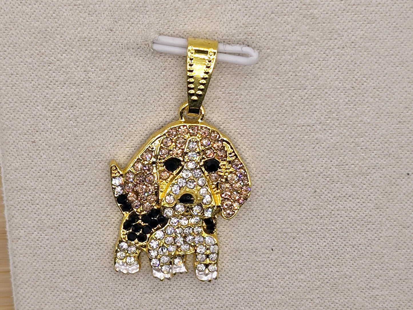 A gold-colored charm in the shape of a dog, adorned with numerous sparkling diamonds.