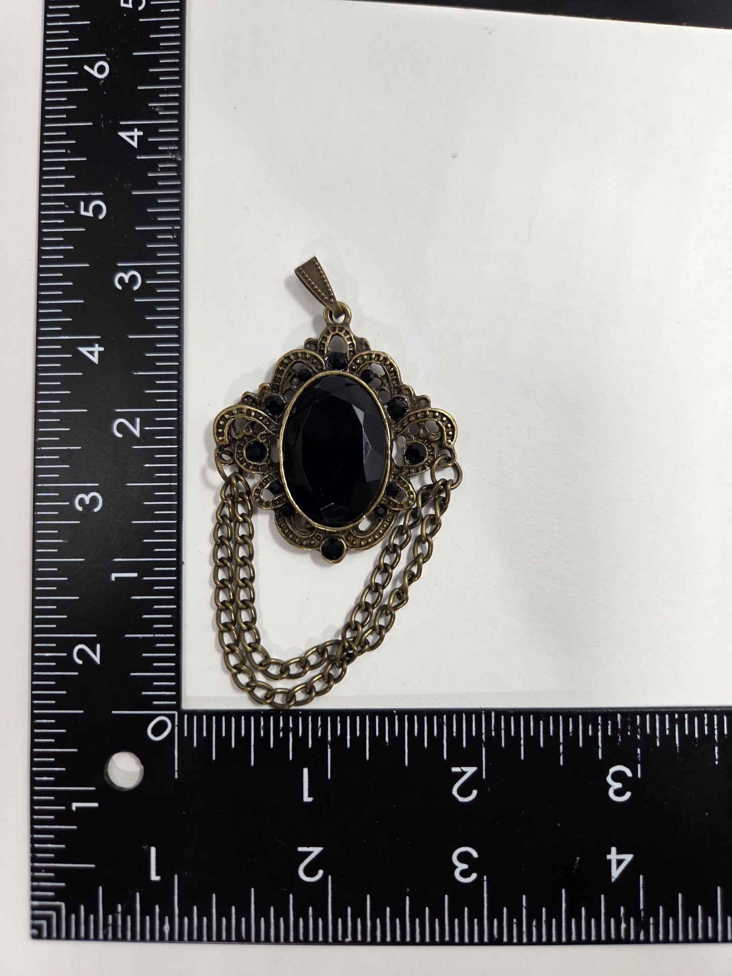a black stone pendant with a decorative metal chain attached to it, placed on a ruler for size comparison.