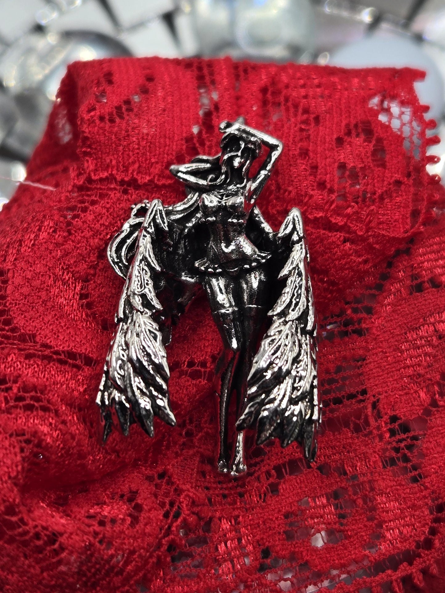 A silver brooch with a winged design is resting on a red lace fabric.