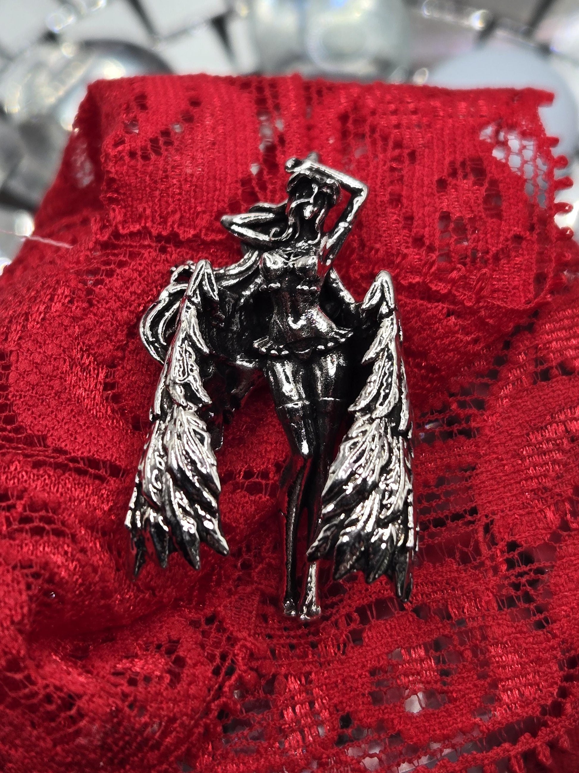 A silver brooch with a winged design is resting on a red lace fabric.