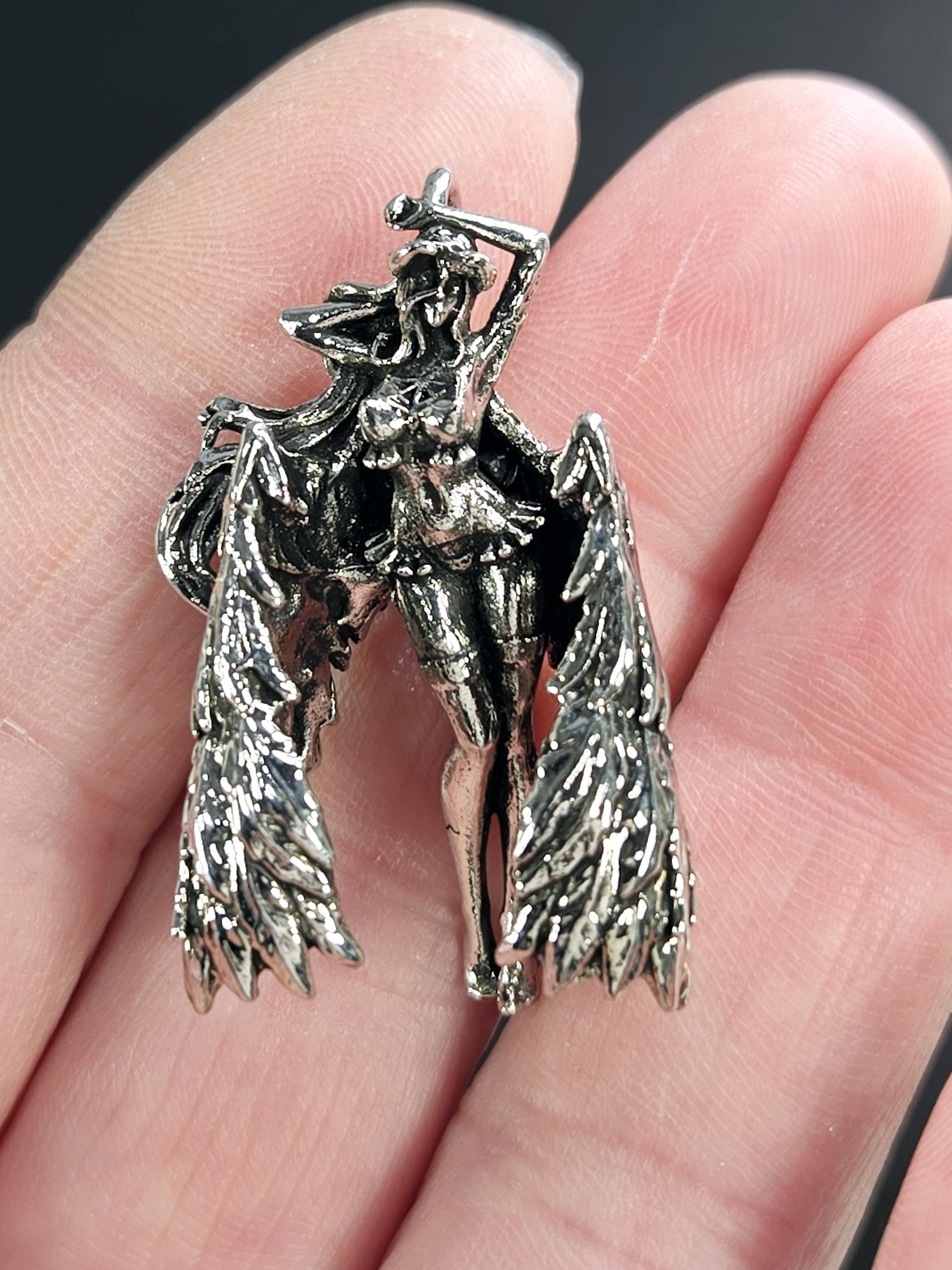 A close-up image of a person's hand holding a small, intricately designed metal sculpture of a winged figure.