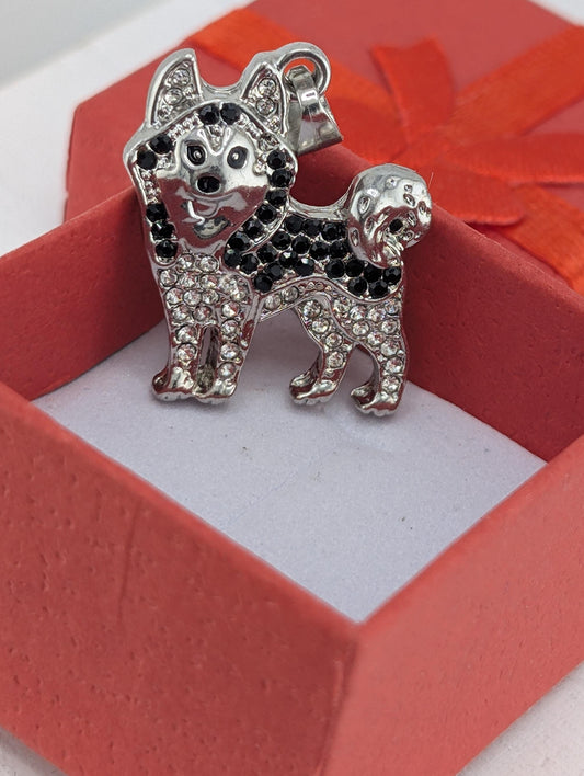 A silver-colored charm in the shape of a dog, adorned with black rhinestones, is displayed inside a red gift box.