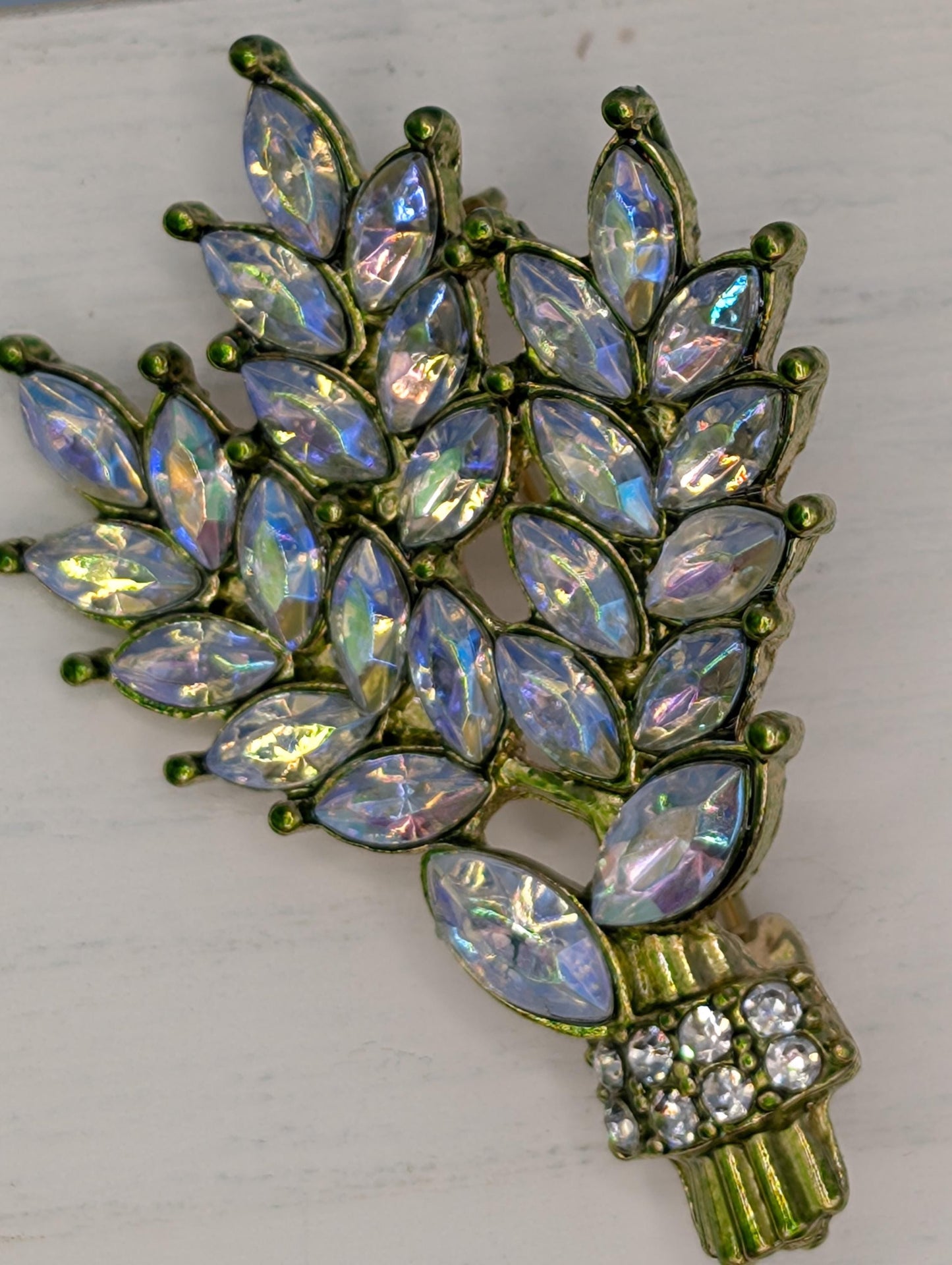 A decorative brooch with a branch-like design, featuring numerous small, clear gemstones in various colors, including blue, green, and purple.