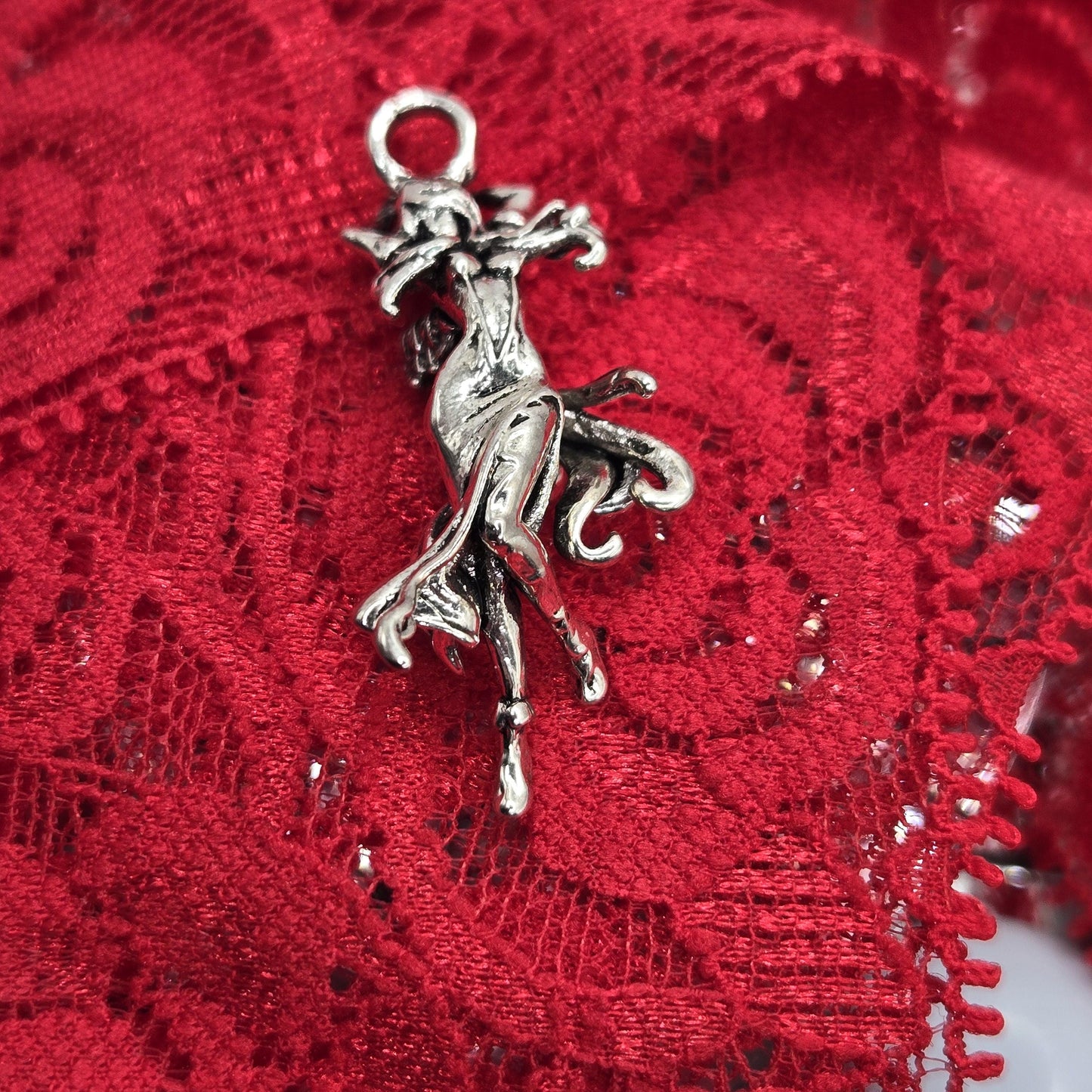 A silver charm in the shape of a bird is resting on a red lace fabric.