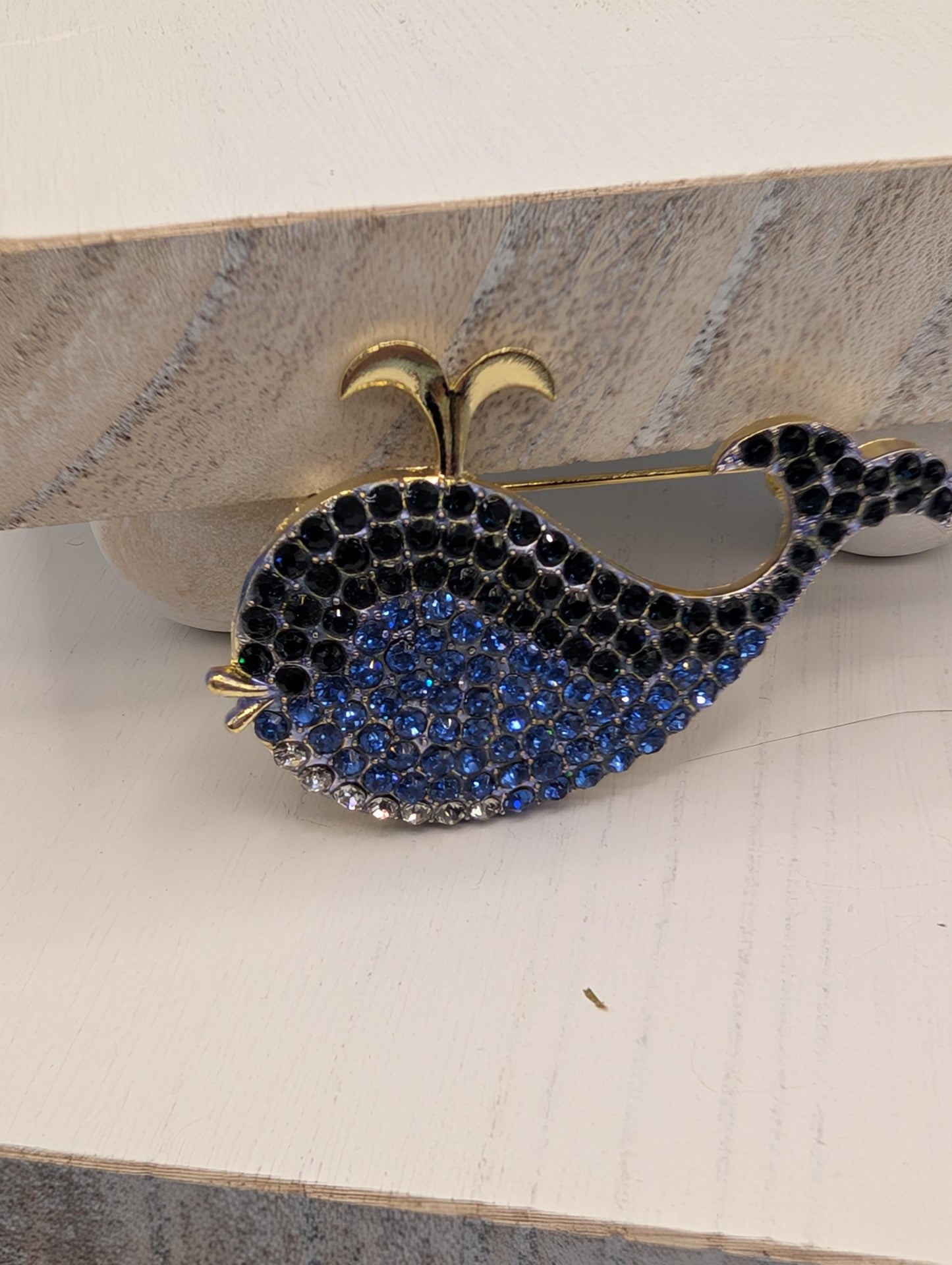 A decorative brooch in the shape of a whale, with a blue and black color scheme and sparkling rhinestones or crystals on its body.