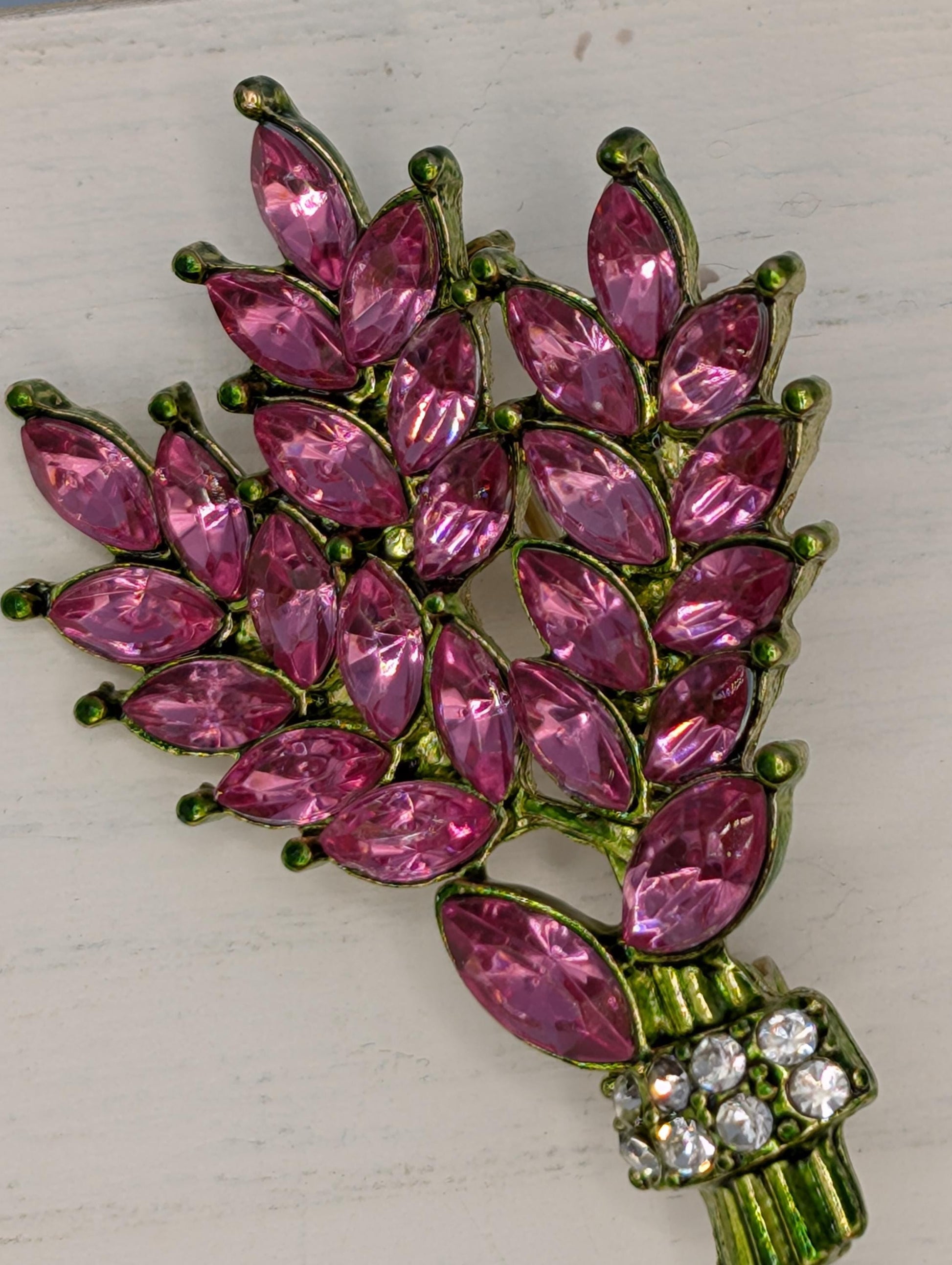 A decorative brooch with a branch-like design, featuring numerous small, pink gemstones or crystals arranged in a floral pattern.