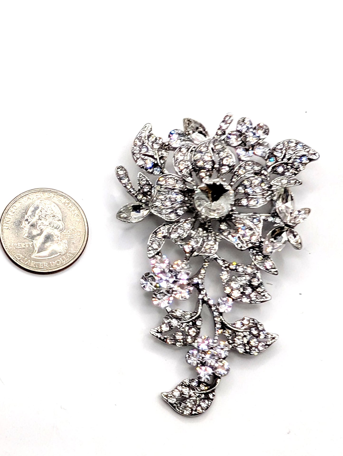 a large, ornate brooch adorned with numerous sparkling crystals and leaves, placed next to a United States quarter coin.