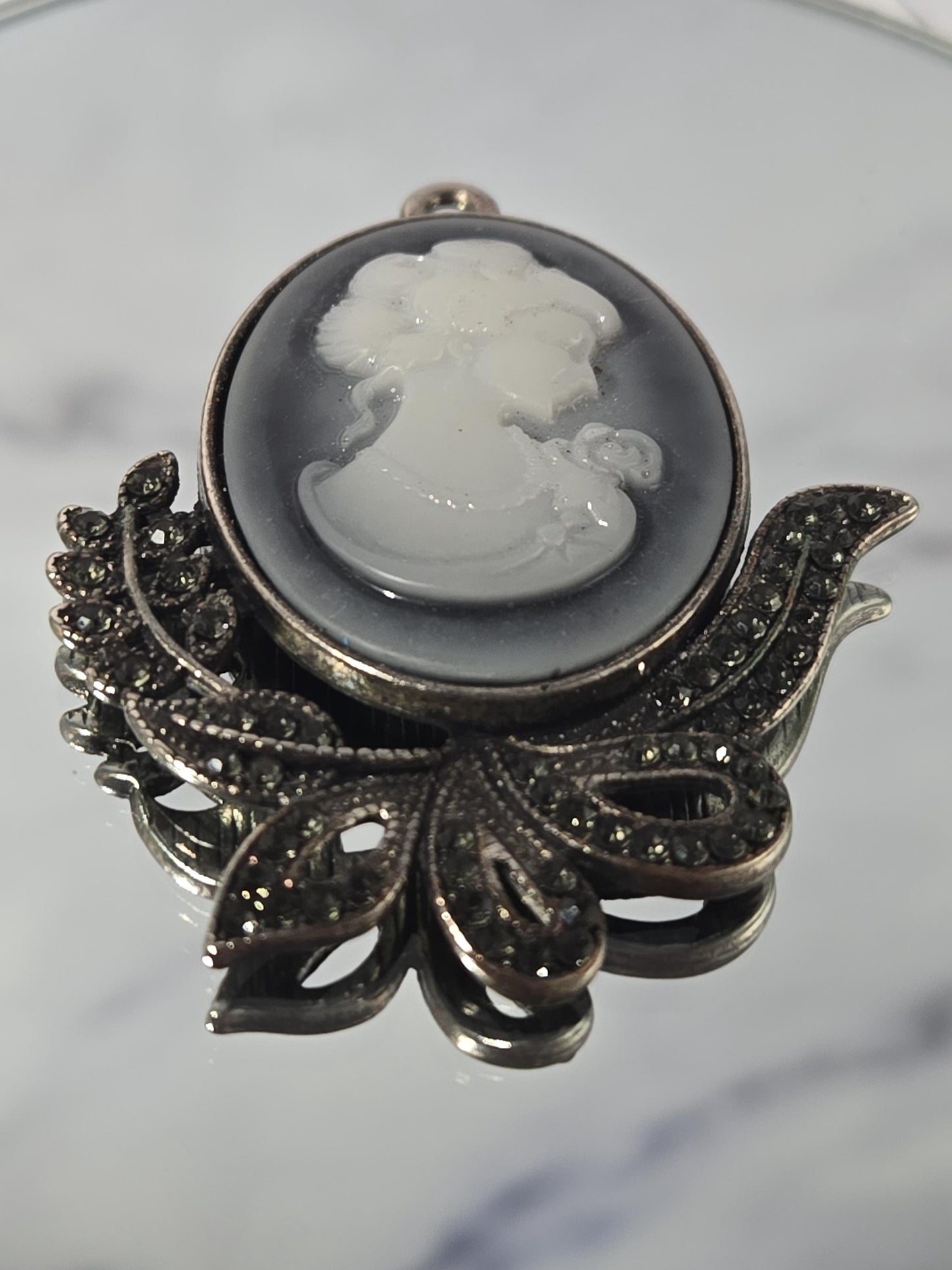 A decorative brooch with a white stone or gemstone in the center, surrounded by intricate metalwork and embellishments.