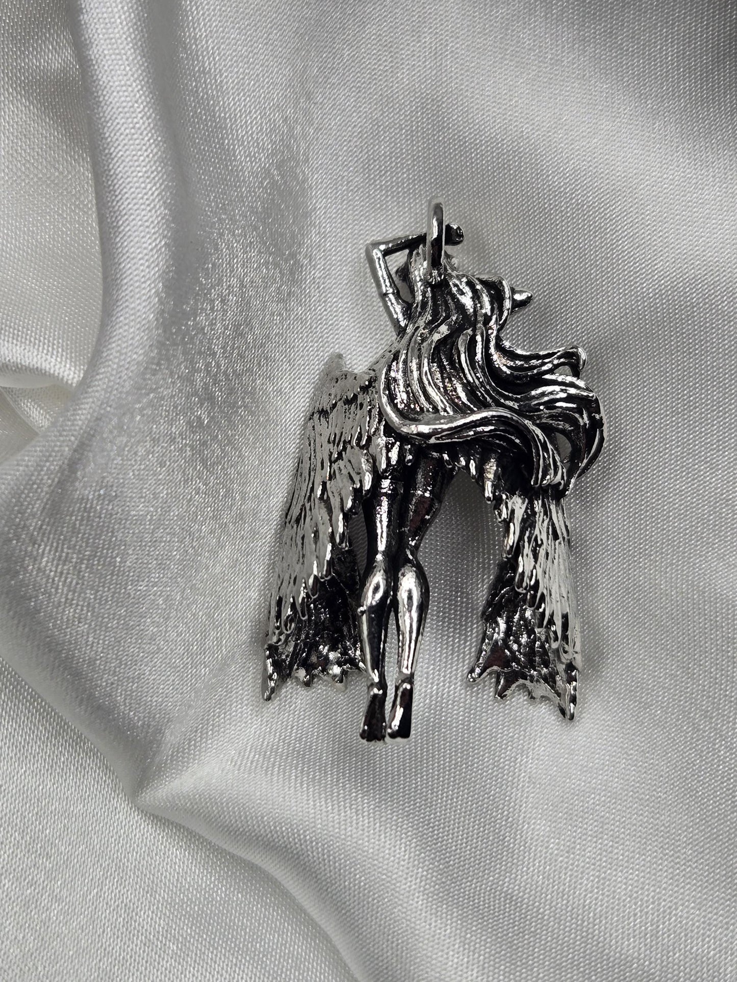 A silver-colored metal brooch in the shape of a winged figure, resting on a white fabric surface.