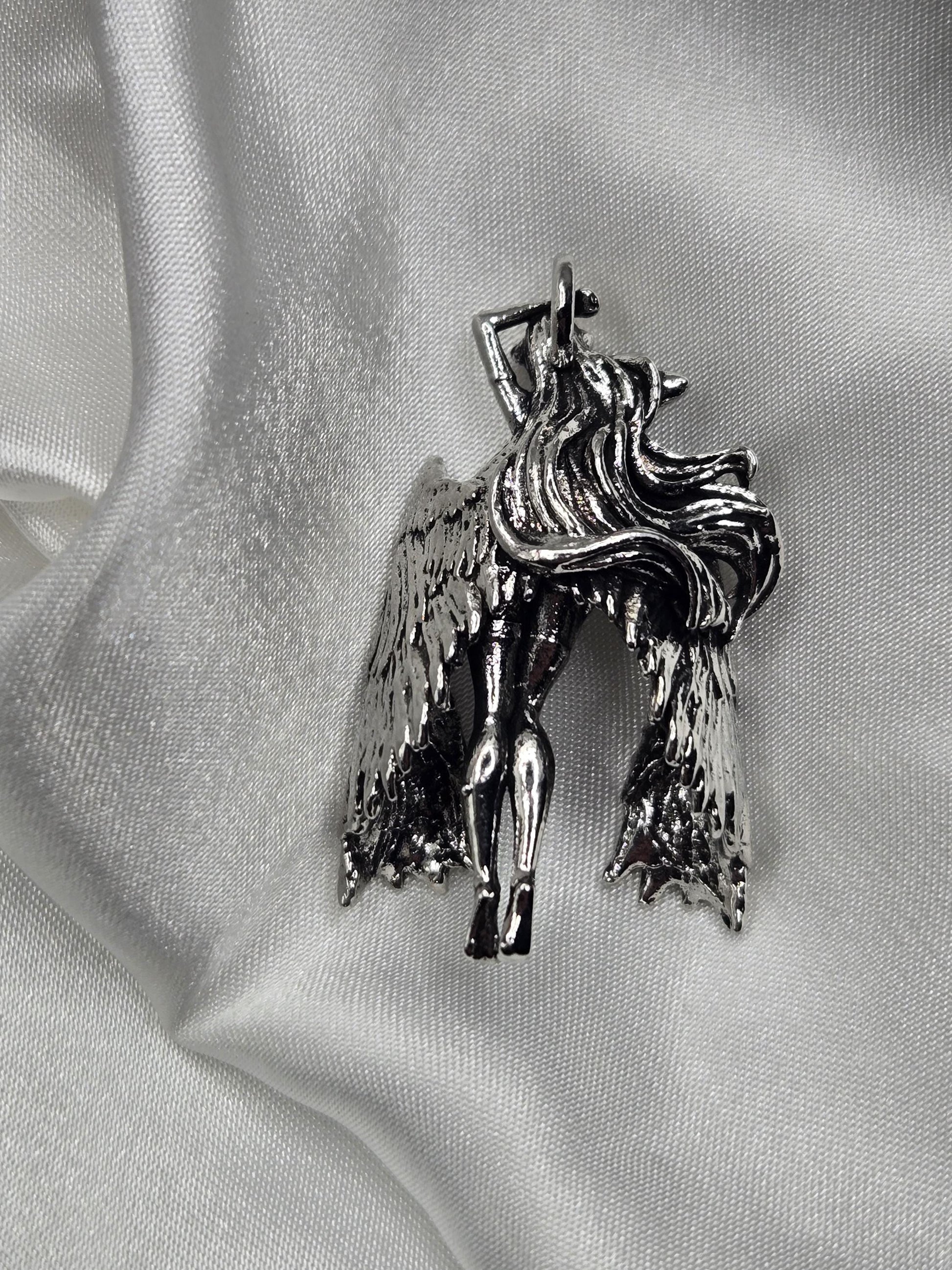 A silver-colored metal brooch in the shape of a winged figure, resting on a white fabric surface.