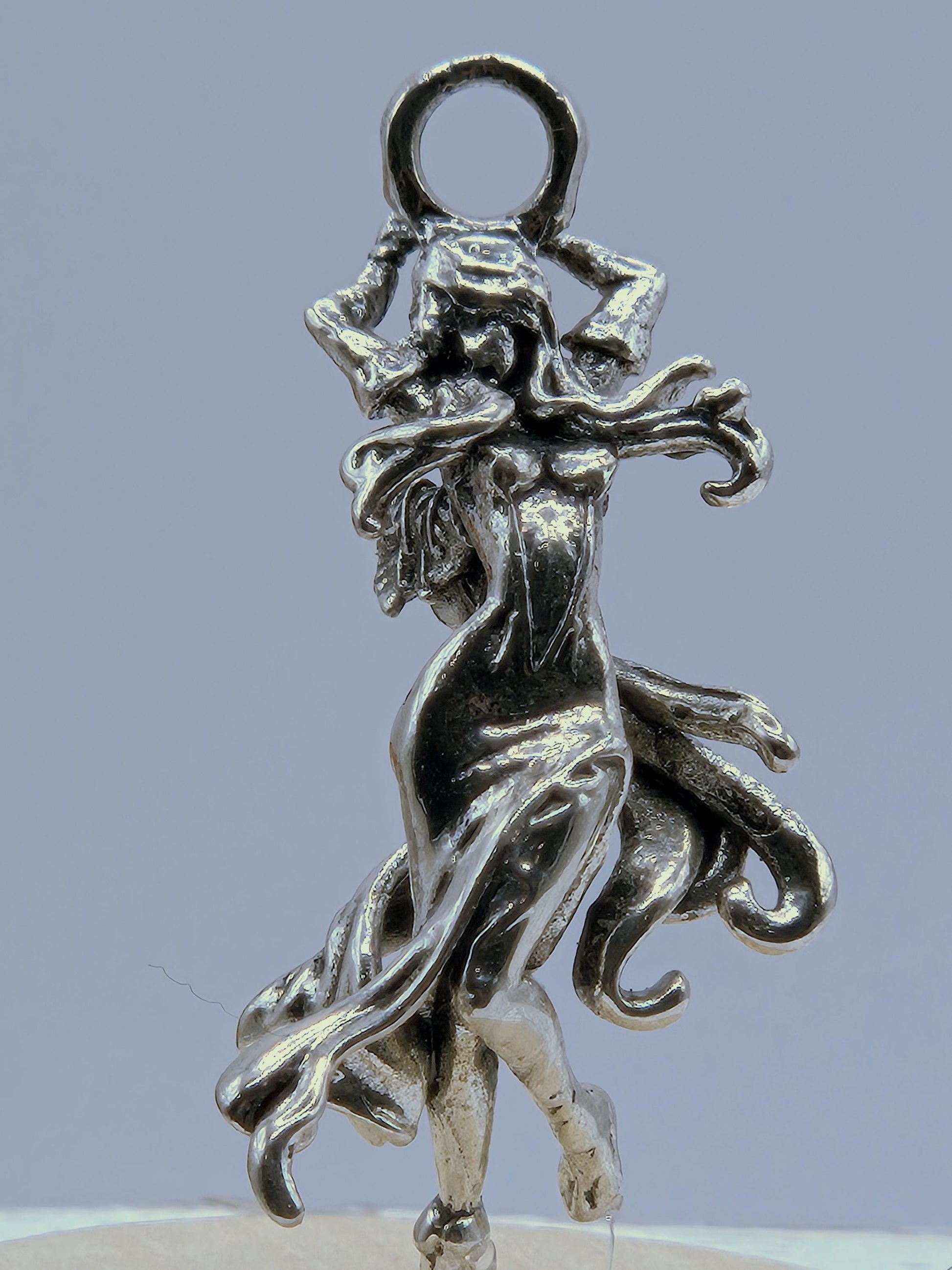 A silver-colored metal charm in the shape of a winged creature, possibly a fairy or dragon, with intricate details and flowing lines.