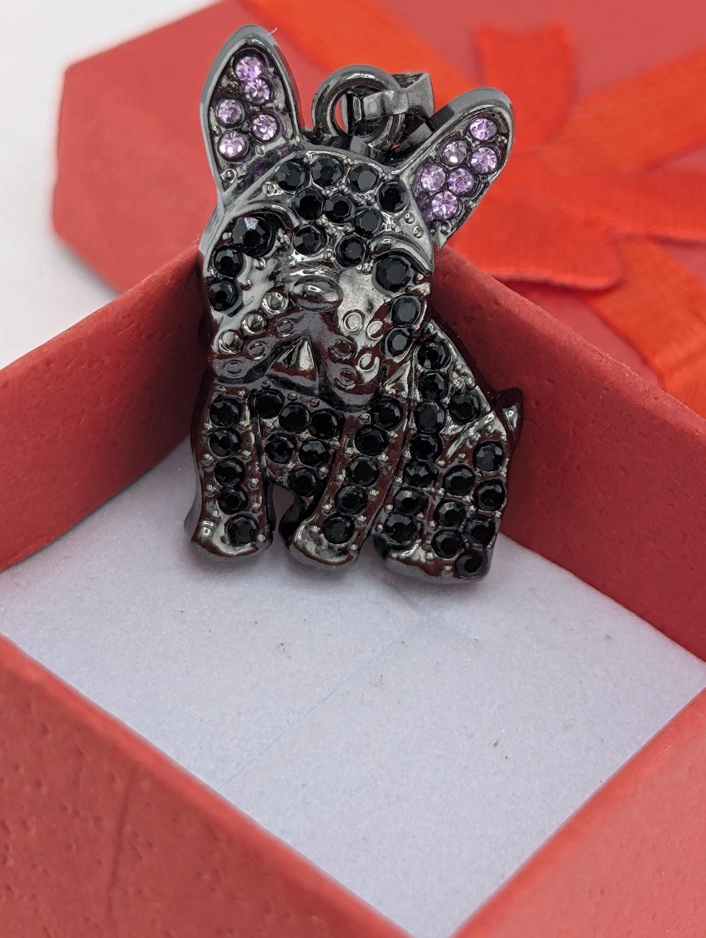 A close-up image of a black dog charm with purple gemstones, displayed in a red box.