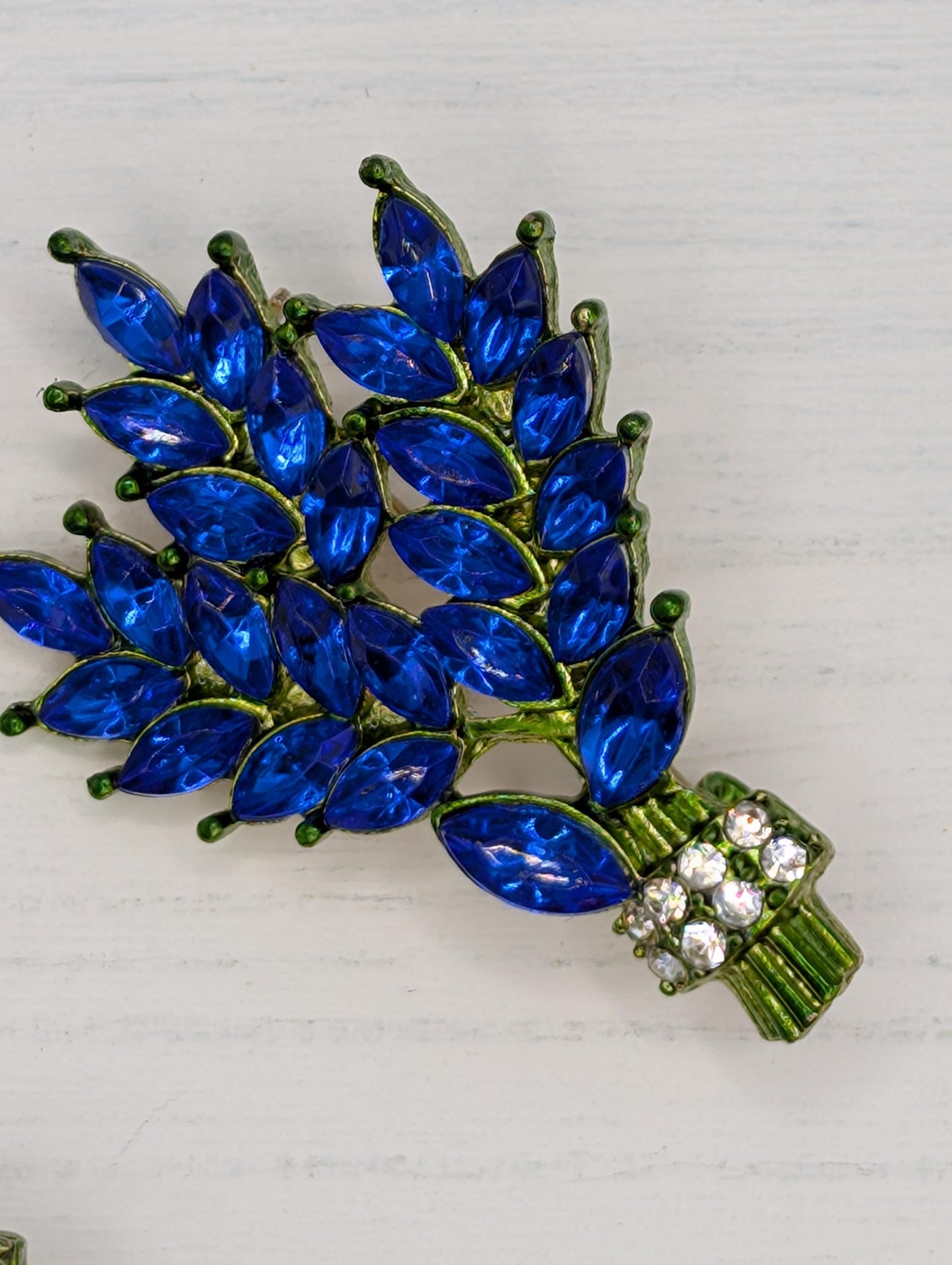 A decorative brooch with blue gemstones and green metal, featuring a cluster of blue gemstones arranged in a stylized manner.