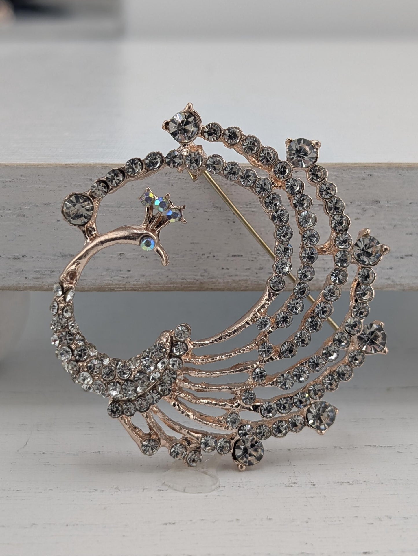 A decorative brooch featuring a peacock design, with intricate details and sparkling crystal elements.