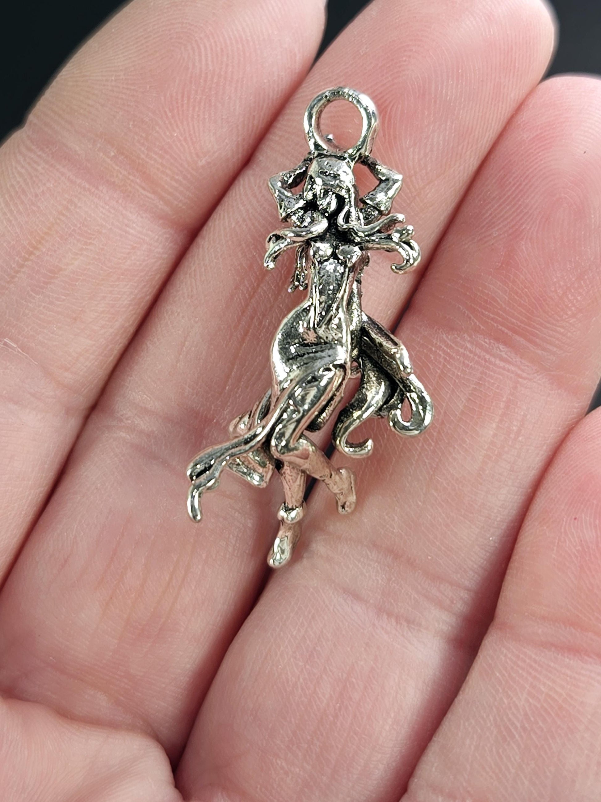 A close-up image of a person's hand holding a small, intricately designed silver charm or pendant.