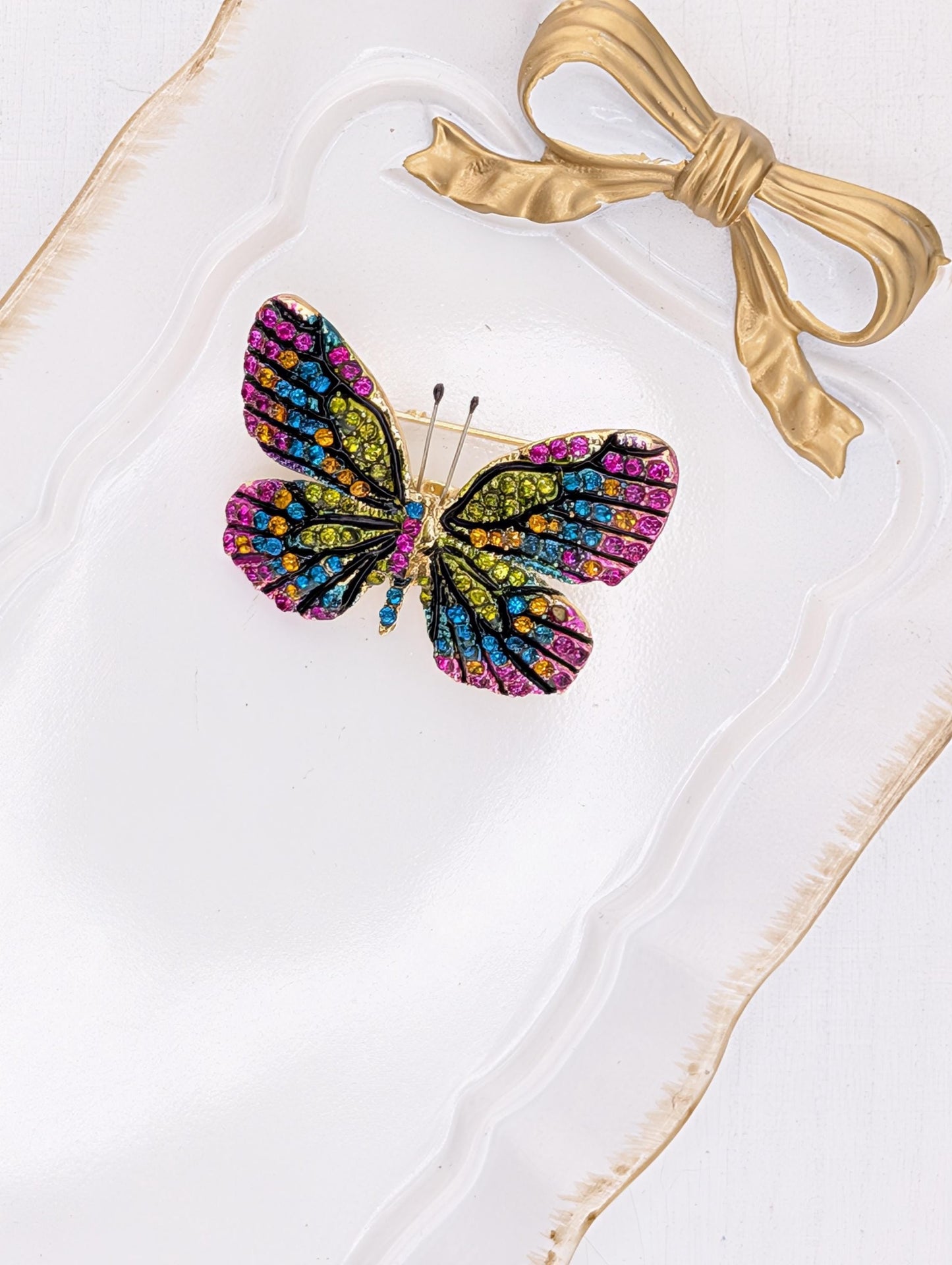 A colorful butterfly brooch with a gold bow on a white background.