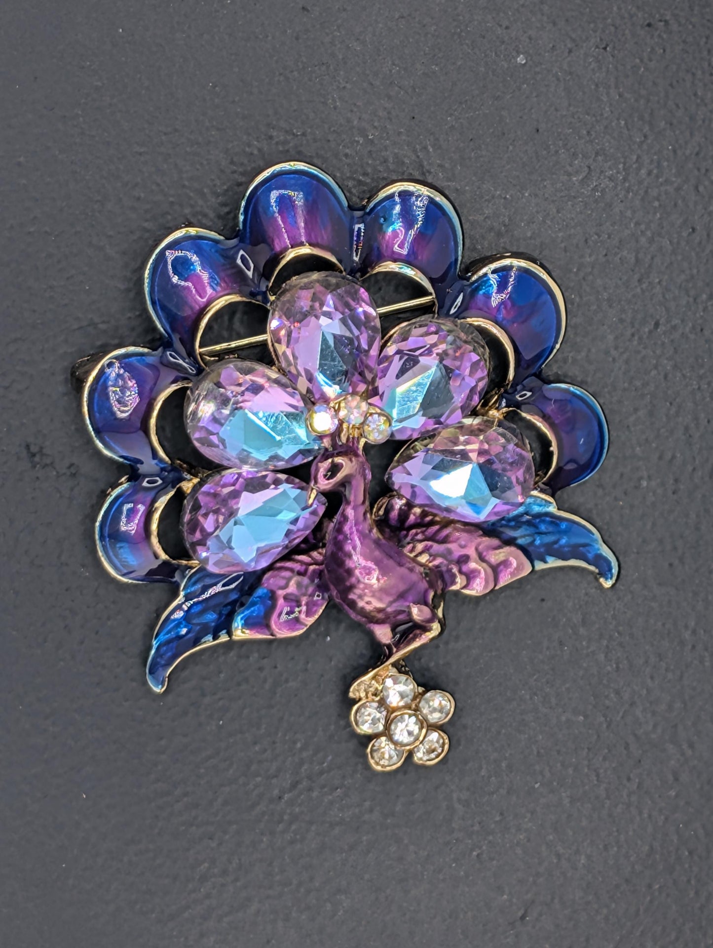 A decorative brooch with a flower-like design, featuring a combination of blue, purple, and pink gemstones, as well as a small cluster of clear gemstones.