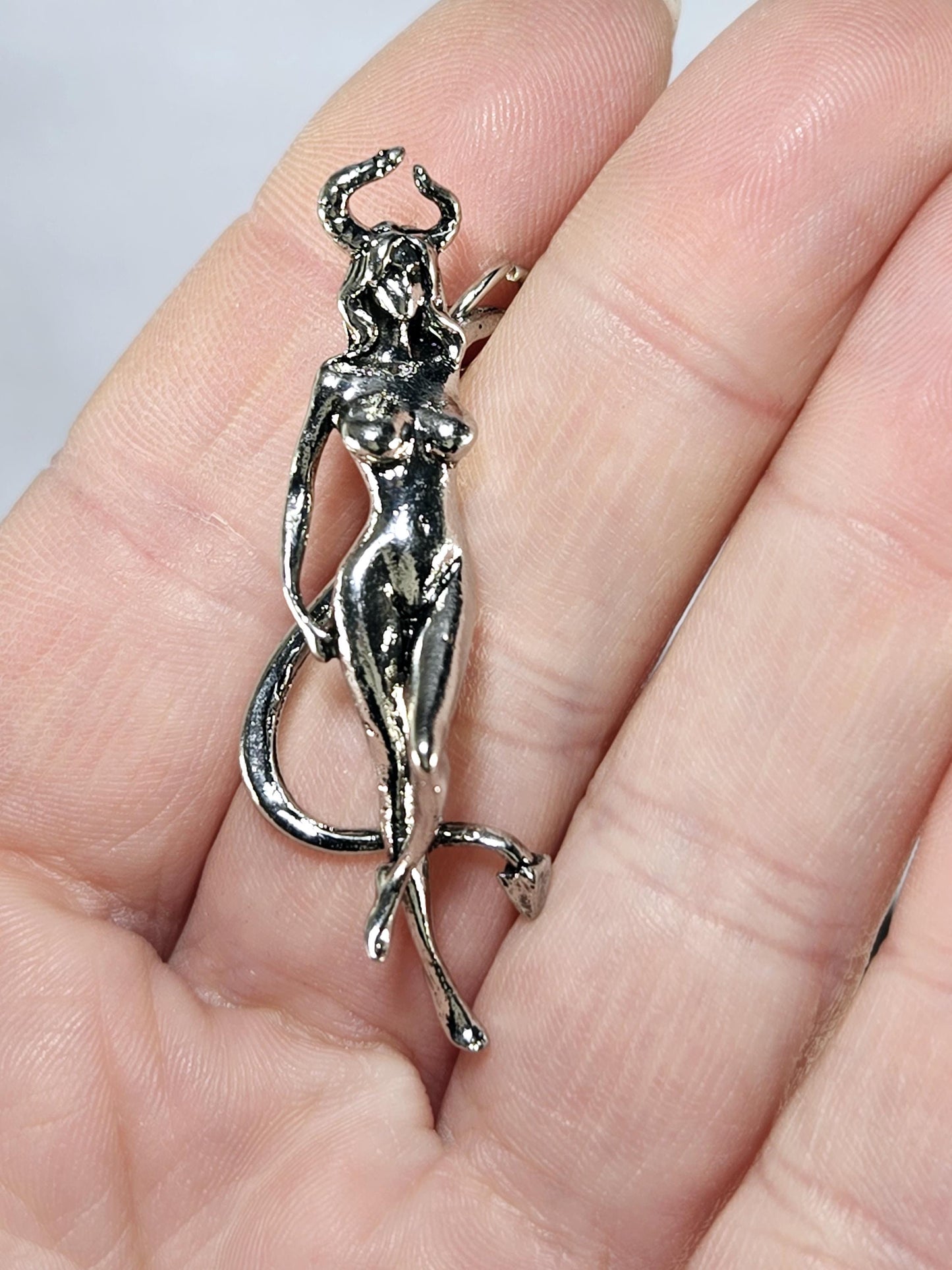 A close-up image of a person's hand holding a silver-colored metal charm or pendant.