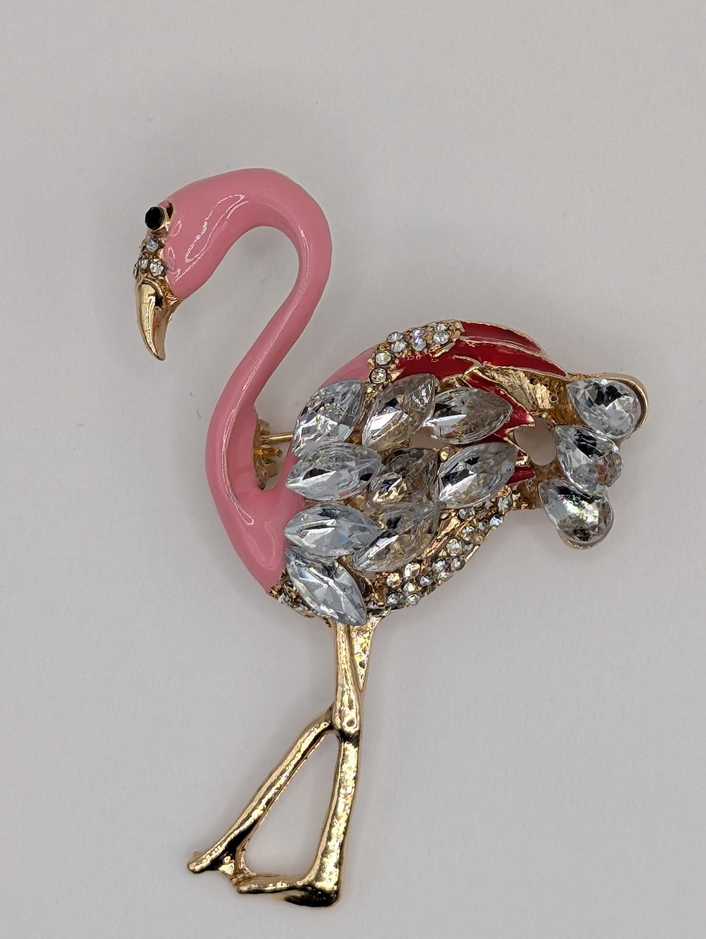A pink flamingo brooch adorned with rhinestones and gold accents.