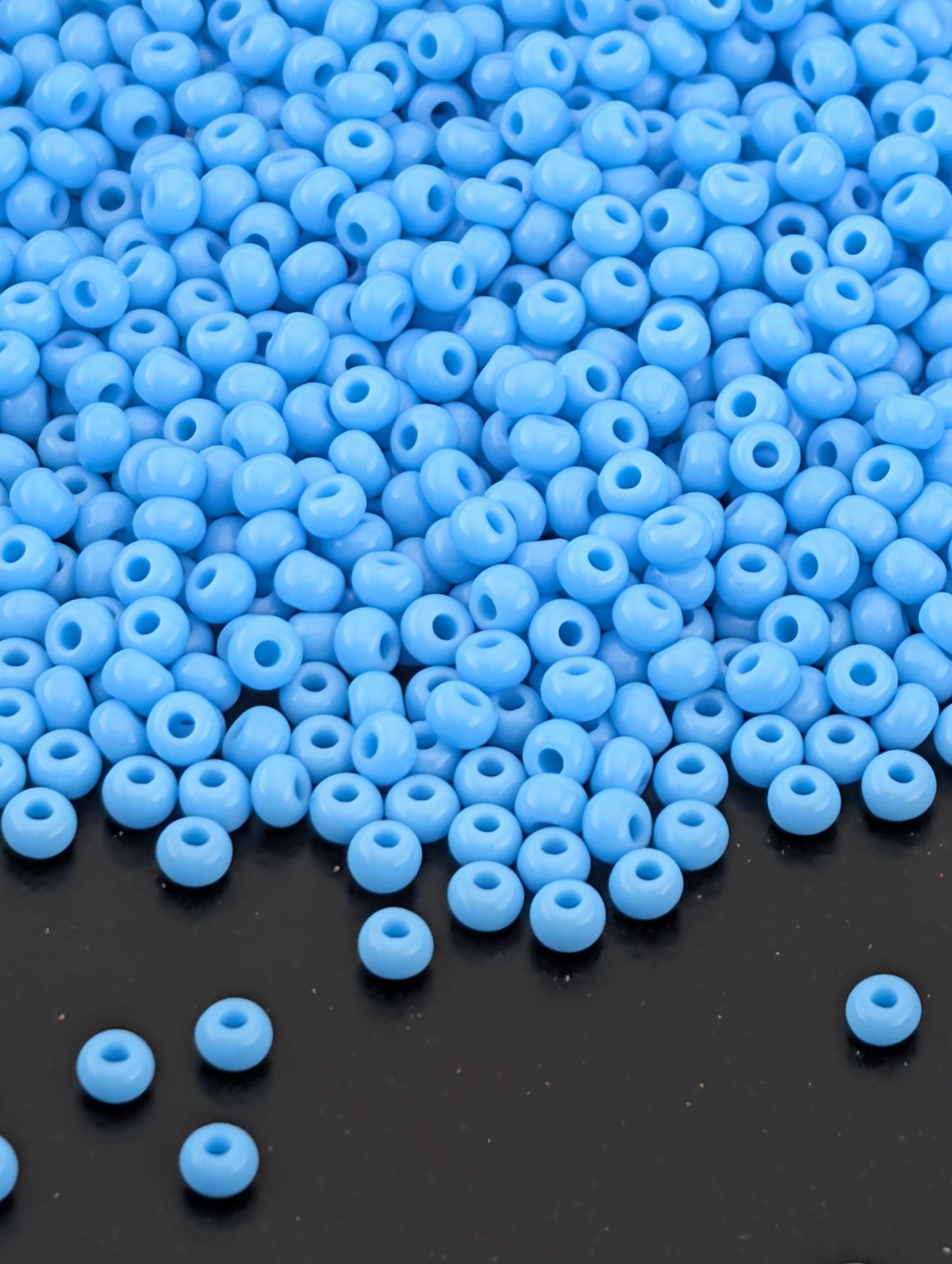 a large pile of small, round blue beads scattered on a dark surface.