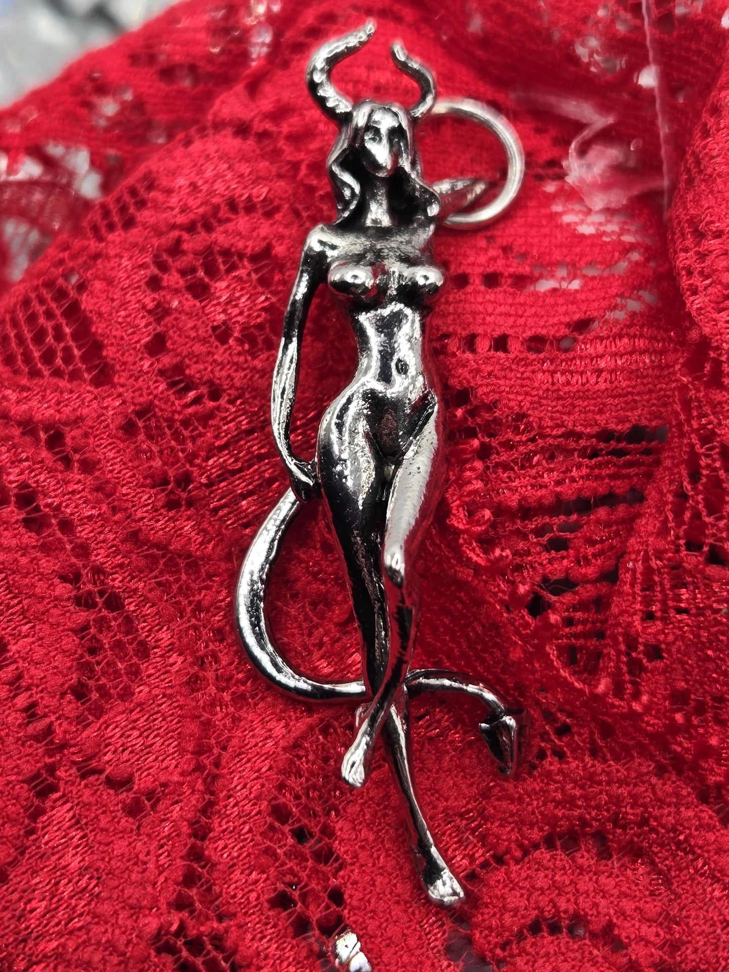A silver metal sculpture of a human figure is displayed on a red lace background.