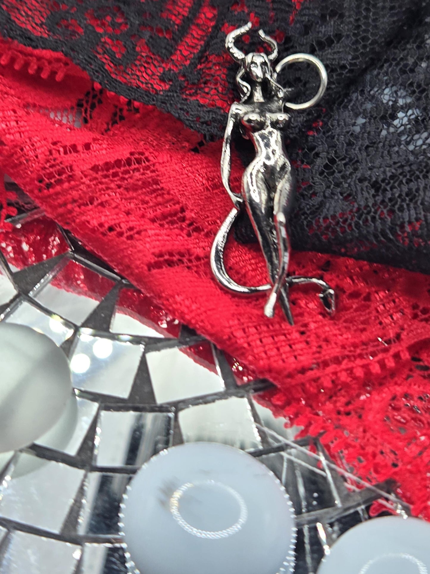 a close-up view of a silver metal object, possibly a piece of jewelry, resting on a red and black fabric. The background is a mosaic of small, reflective surfaces, creating a visually striking contrast with the metallic object.
