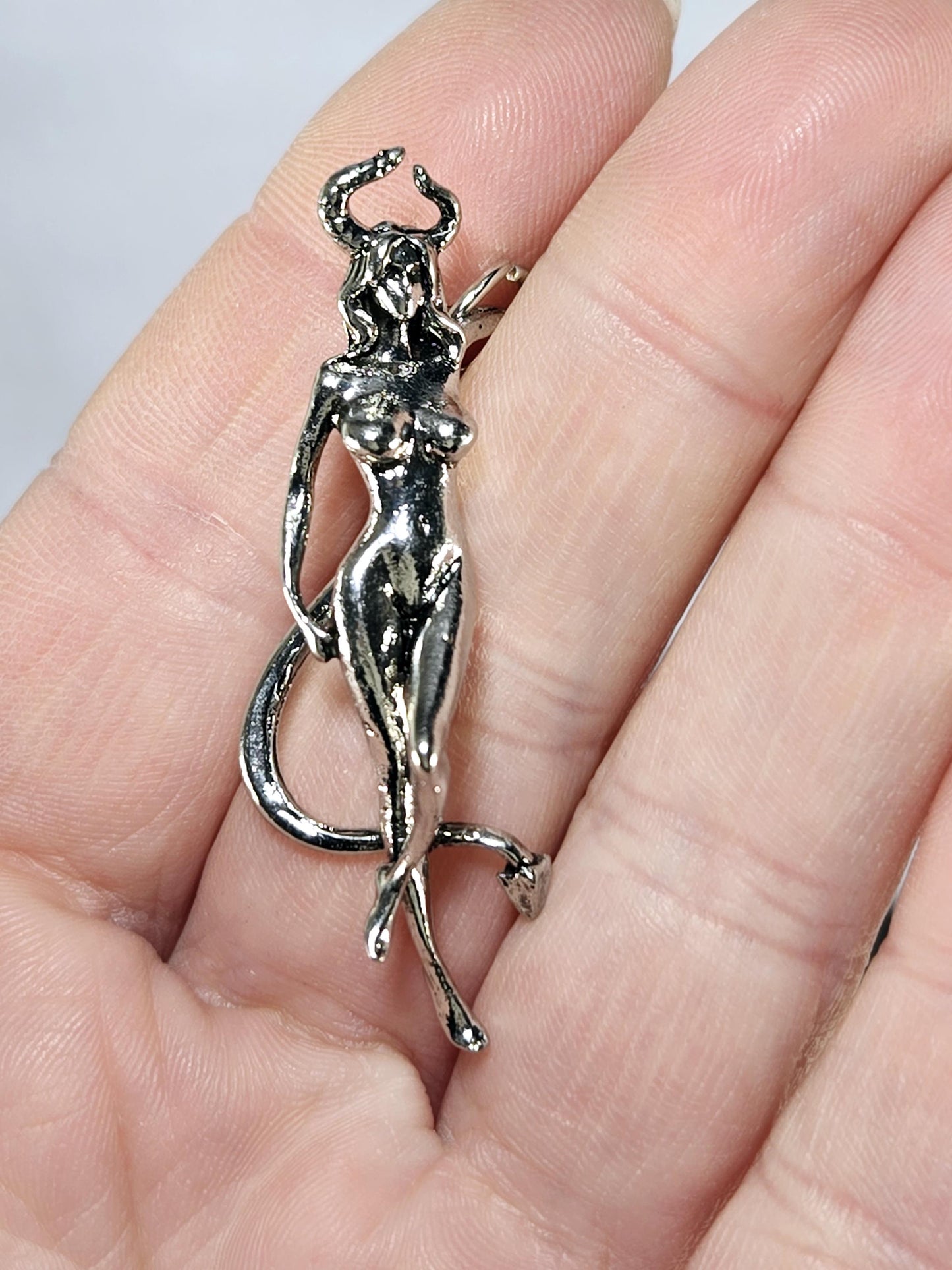 A close-up image of a person's hand holding a silver-colored metal charm or pendant.