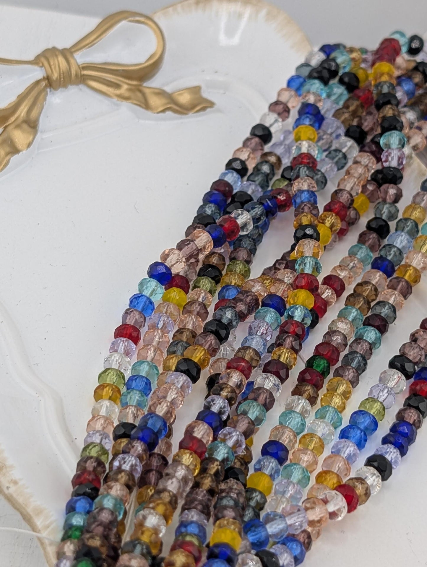 A collection of colorful glass beads arranged on a white surface, with a gold bow in the background.