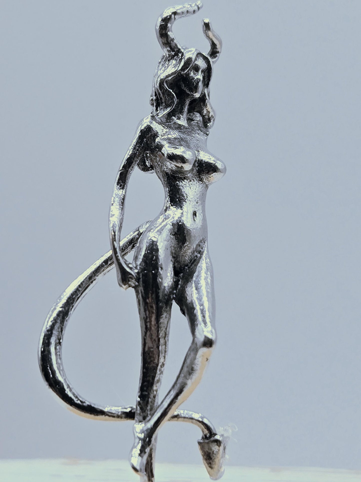 A silver-colored metal sculpture of a human figure, with a twisted and distorted appearance, is shown against a light blue background.