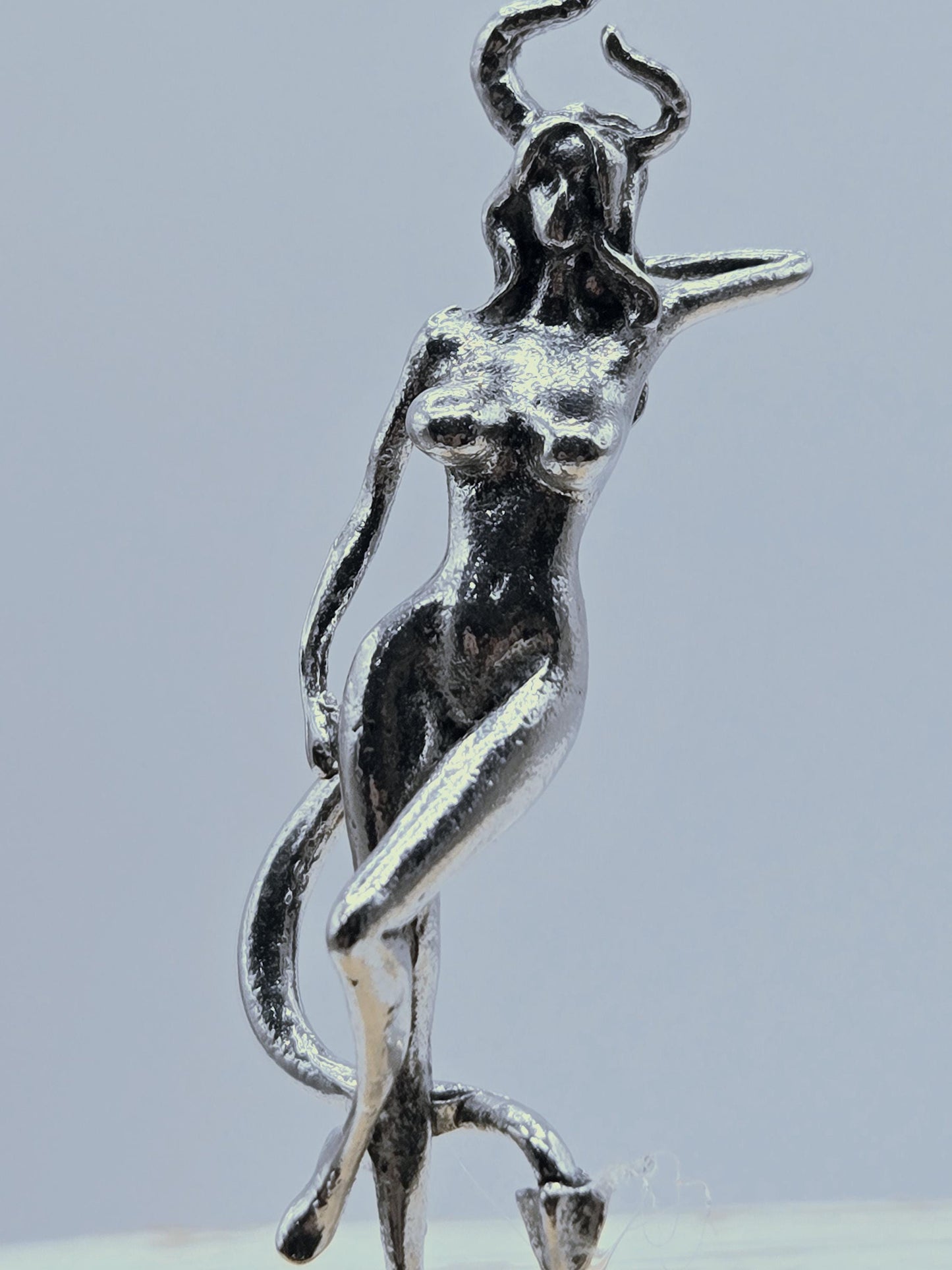 A silver-colored metal sculpture of a human figure, with a twisted and distorted form, is shown against a light blue background.