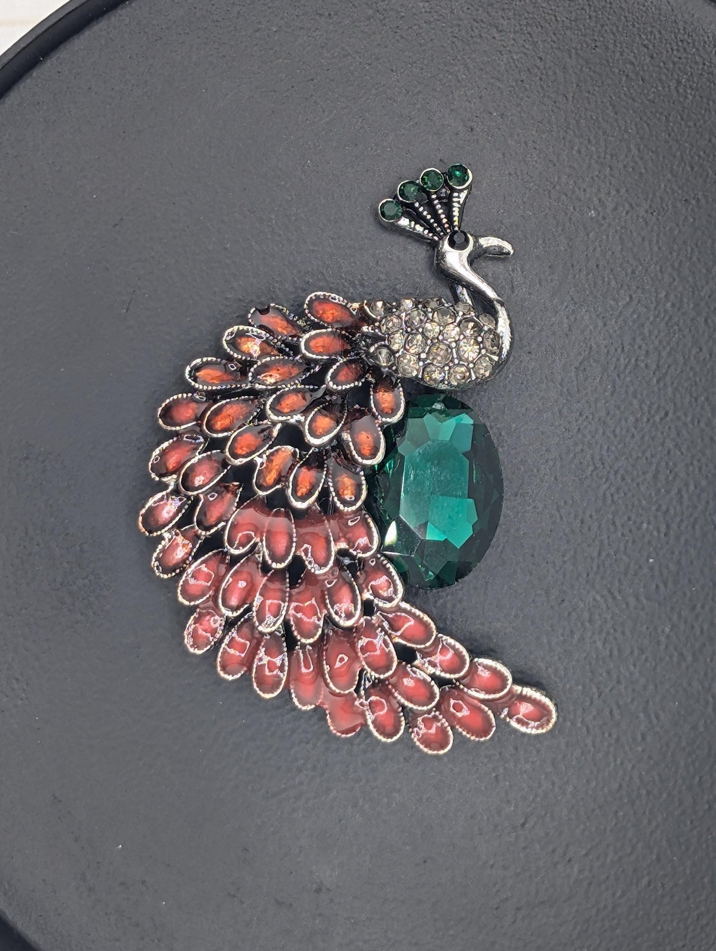 A decorative brooch with a large green gemstone and a pattern of red and orange gemstones.
