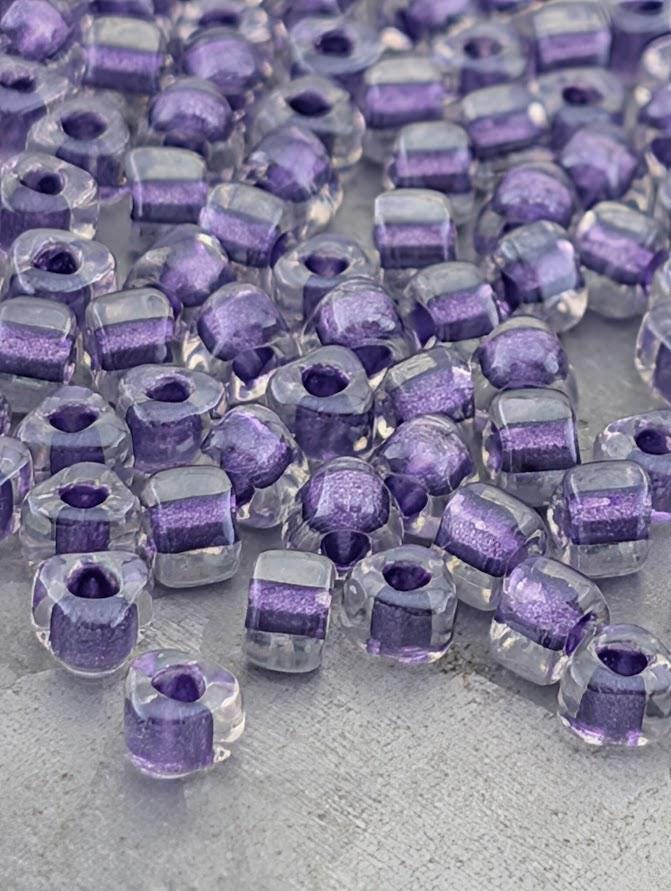 a collection of clear glass beads in various shades of purple, scattered across a surface.