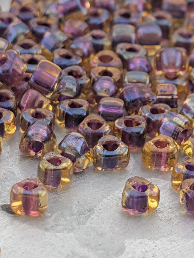 a collection of colorful glass beads scattered on a surface, with various shades of purple, yellow, and orange.