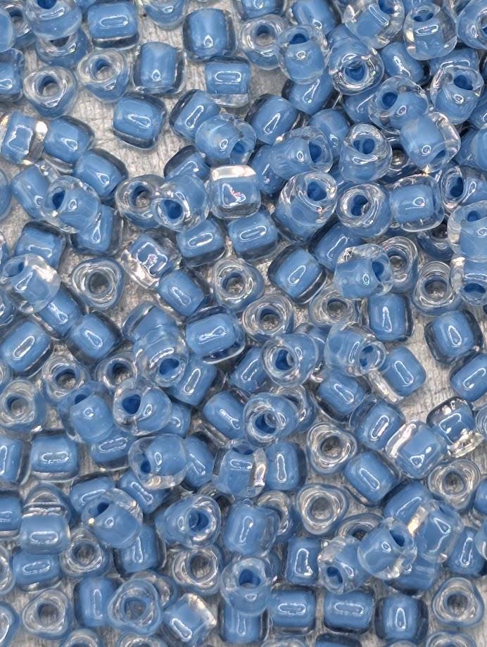 The image is a close-up of numerous small, clear beads in various shades of blue, scattered across a surface.