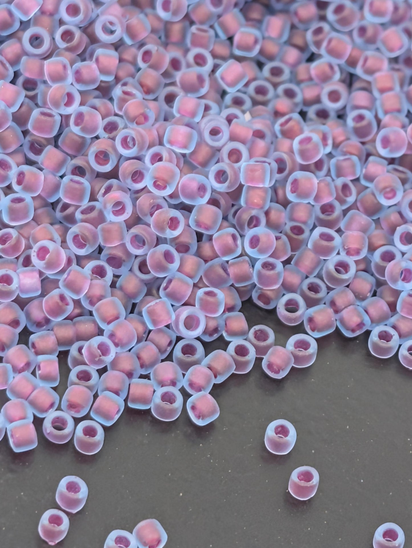 a large pile of small, clear beads in various shades of pink and purple, scattered across a dark surface.