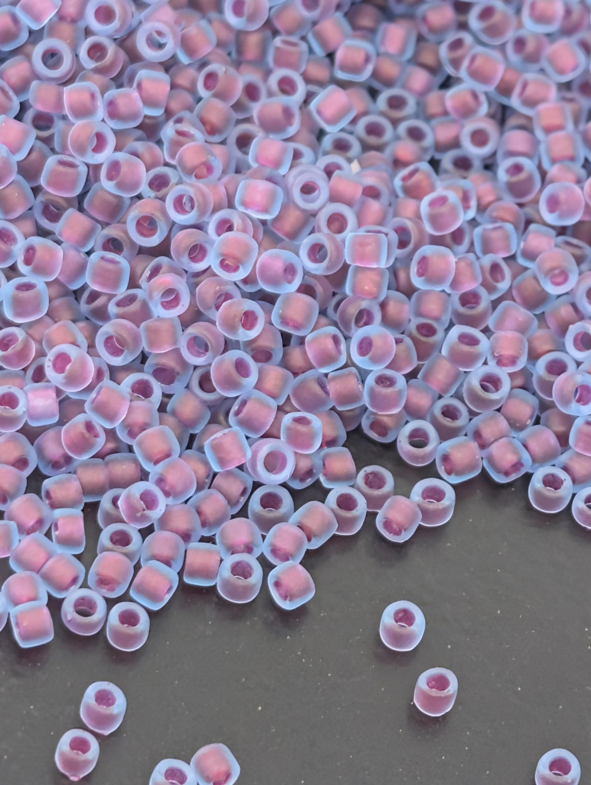 a large pile of small, clear beads in various shades of pink and purple, scattered across a dark surface.