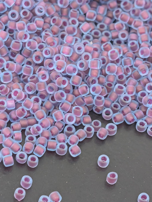 a large pile of small, clear beads in various shades of pink and purple, scattered across a dark surface.