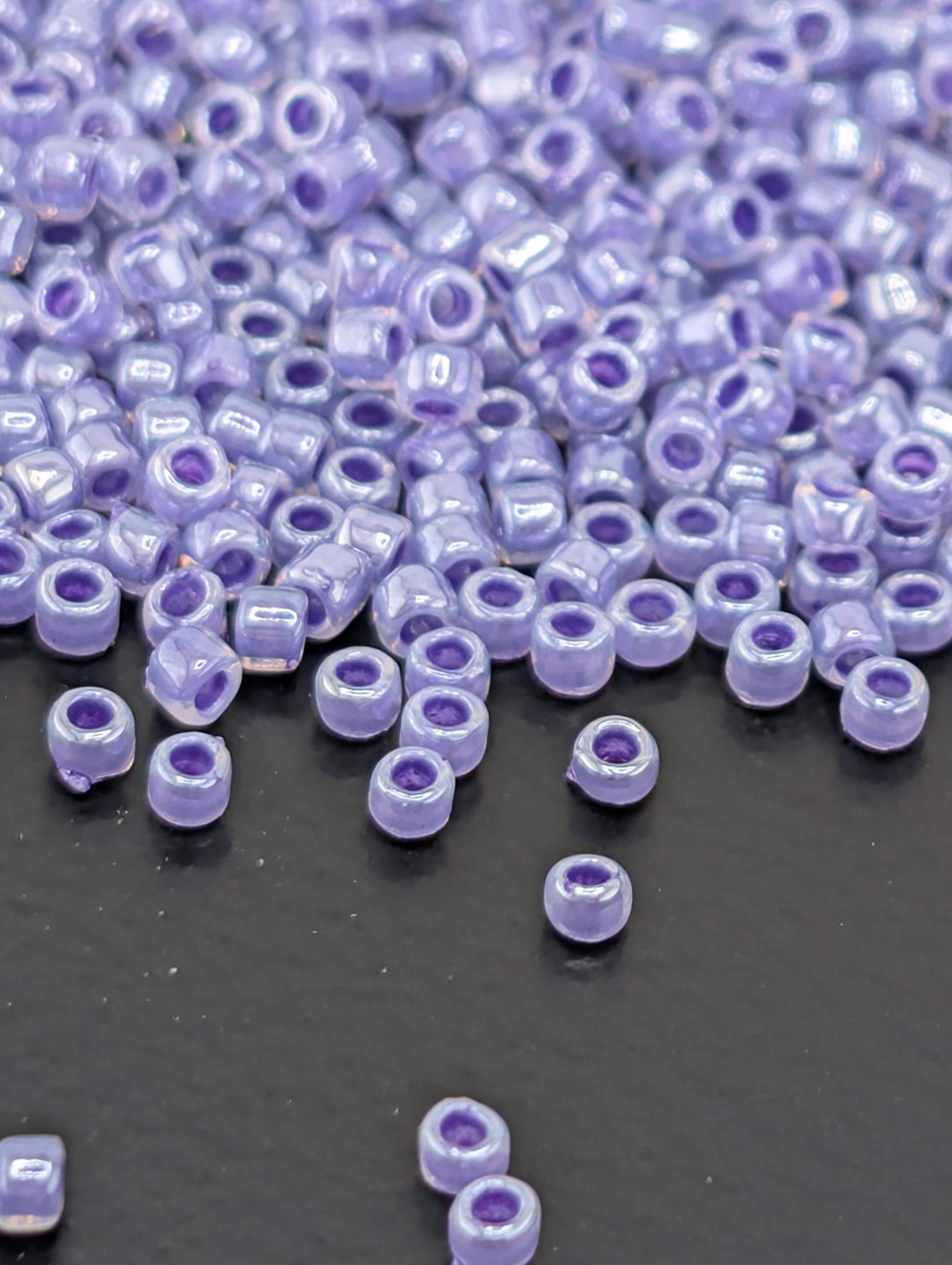 a close-up view of numerous small, round beads in various shades of purple, scattered across a dark surface.