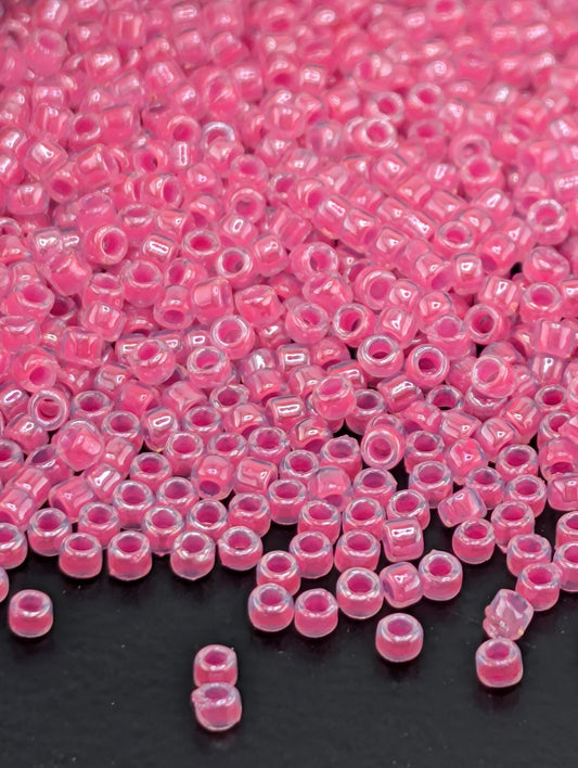 a large pile of small, clear beads in a vibrant shade of pink, scattered across a dark surface.