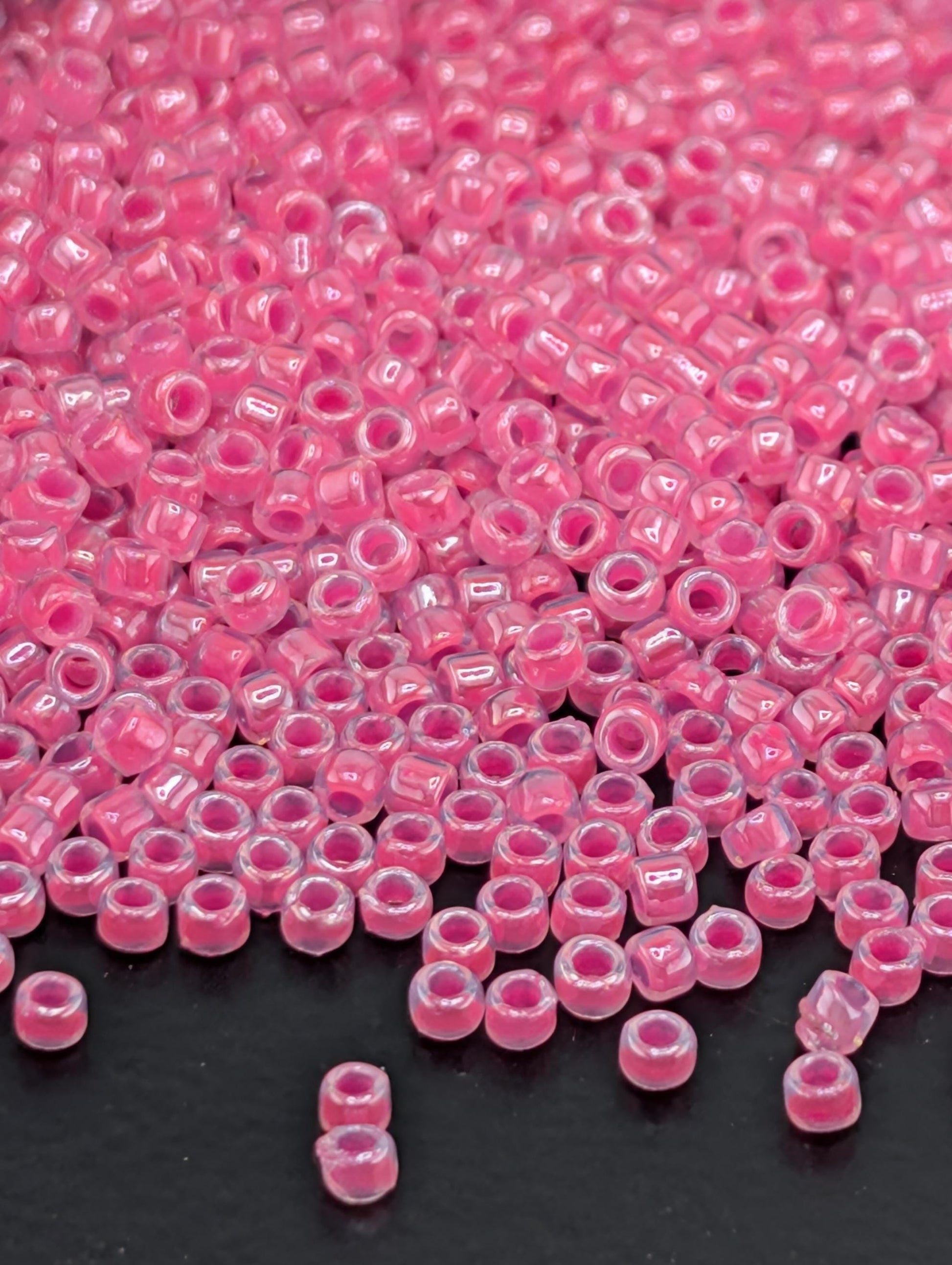 a large pile of small, clear beads in a vibrant shade of pink, scattered across a dark surface.