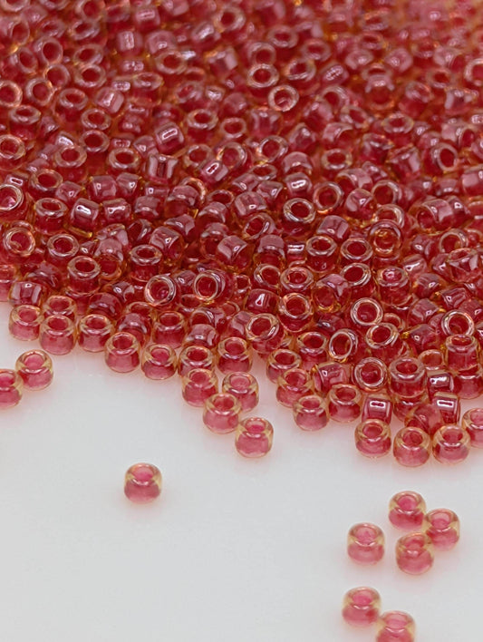 a close-up view of numerous small, clear beads in a vibrant red color, scattered across a white surface.