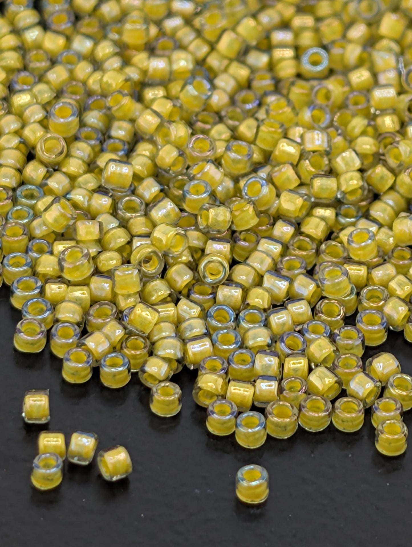 a large pile of small, yellow beads scattered on a dark surface.