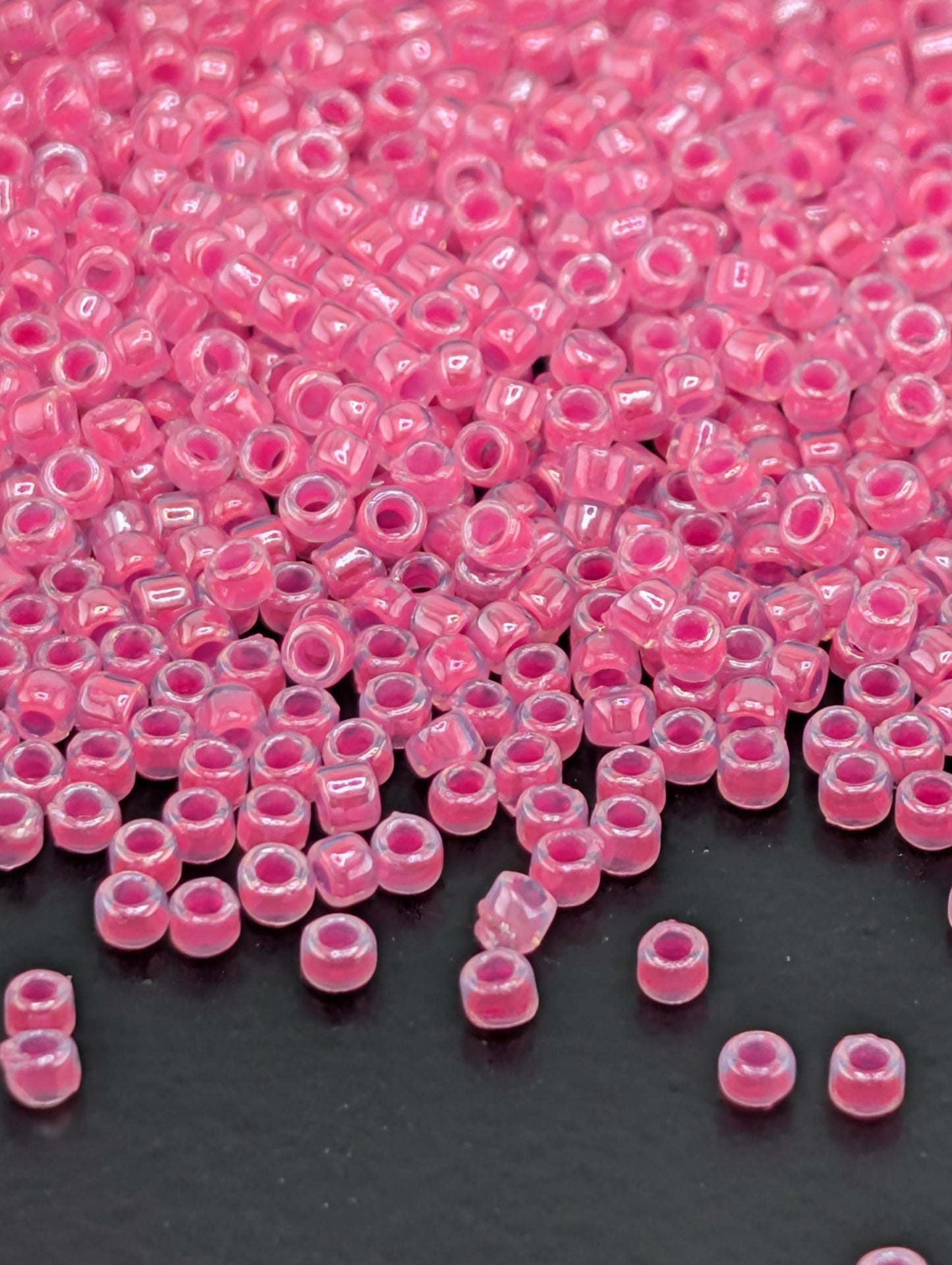 a close-up view of numerous small, clear beads in a vibrant shade of pink, scattered across a dark background.