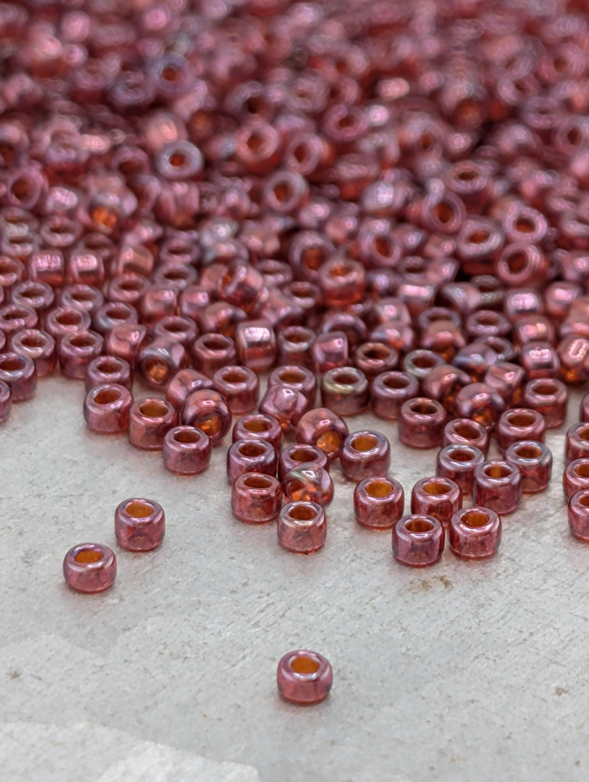 a large pile of small, round, metallic beads in various shades of red and orange, scattered across a surface.