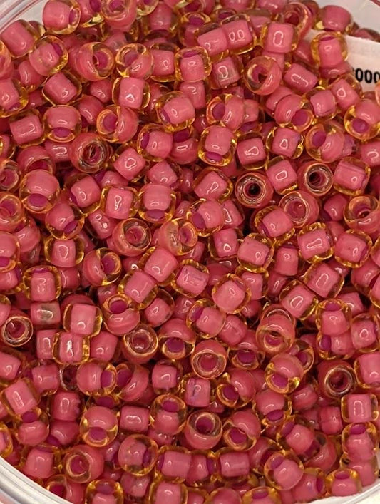 A close-up image of a large pile of small, clear beads in shades of pink and yellow.