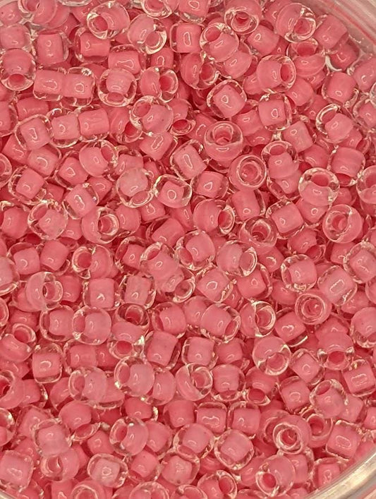 A close-up image of a container filled with numerous small, clear beads in a vibrant shade of pink.