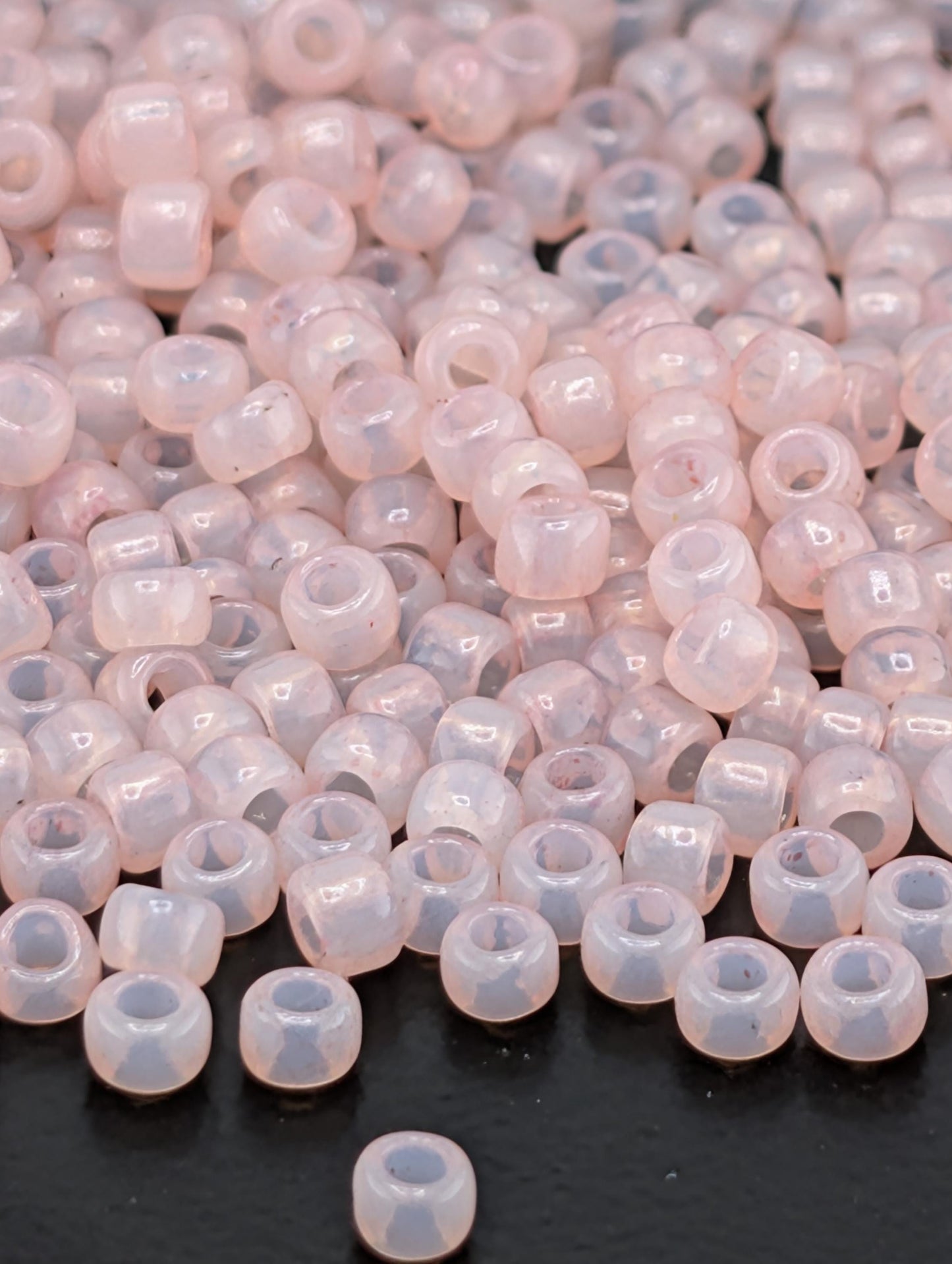 a large pile of small, clear beads in various shades of pink and white, scattered on a dark surface.