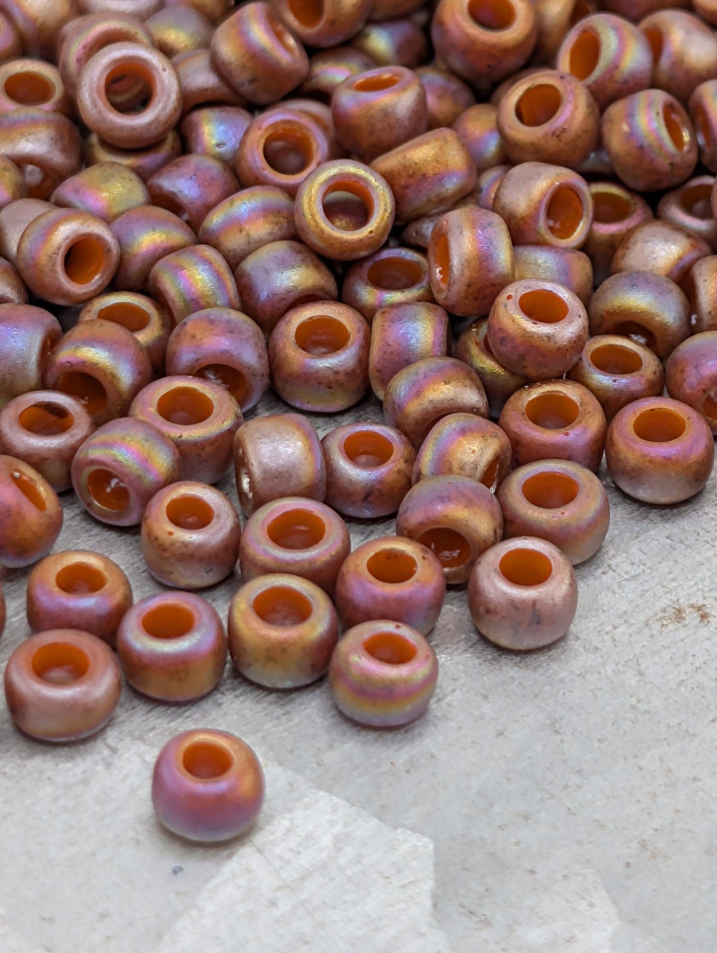 a large pile of multicolored beads, including small orange and pink beads, scattered on a surface.
