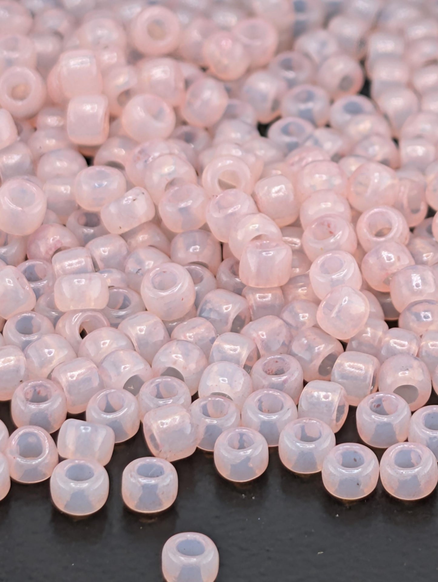 A close-up image of numerous small, clear beads in various shades of pink and white, scattered on a dark surface.