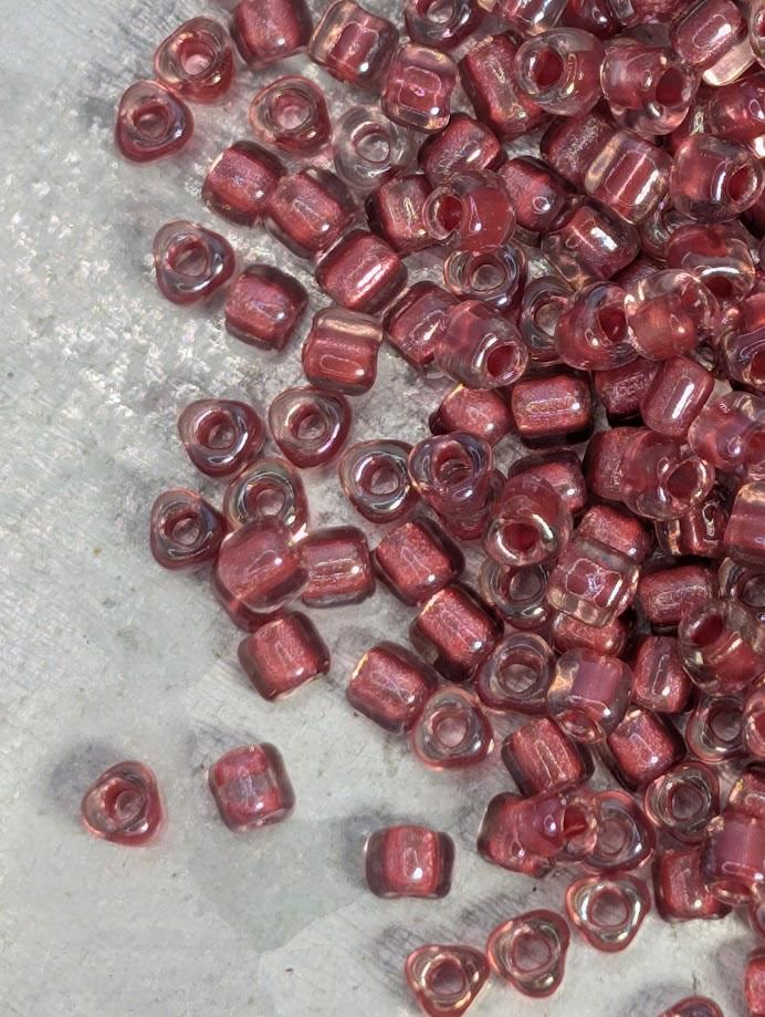 a collection of small, clear beads in various shades of red, scattered on a textured surface.